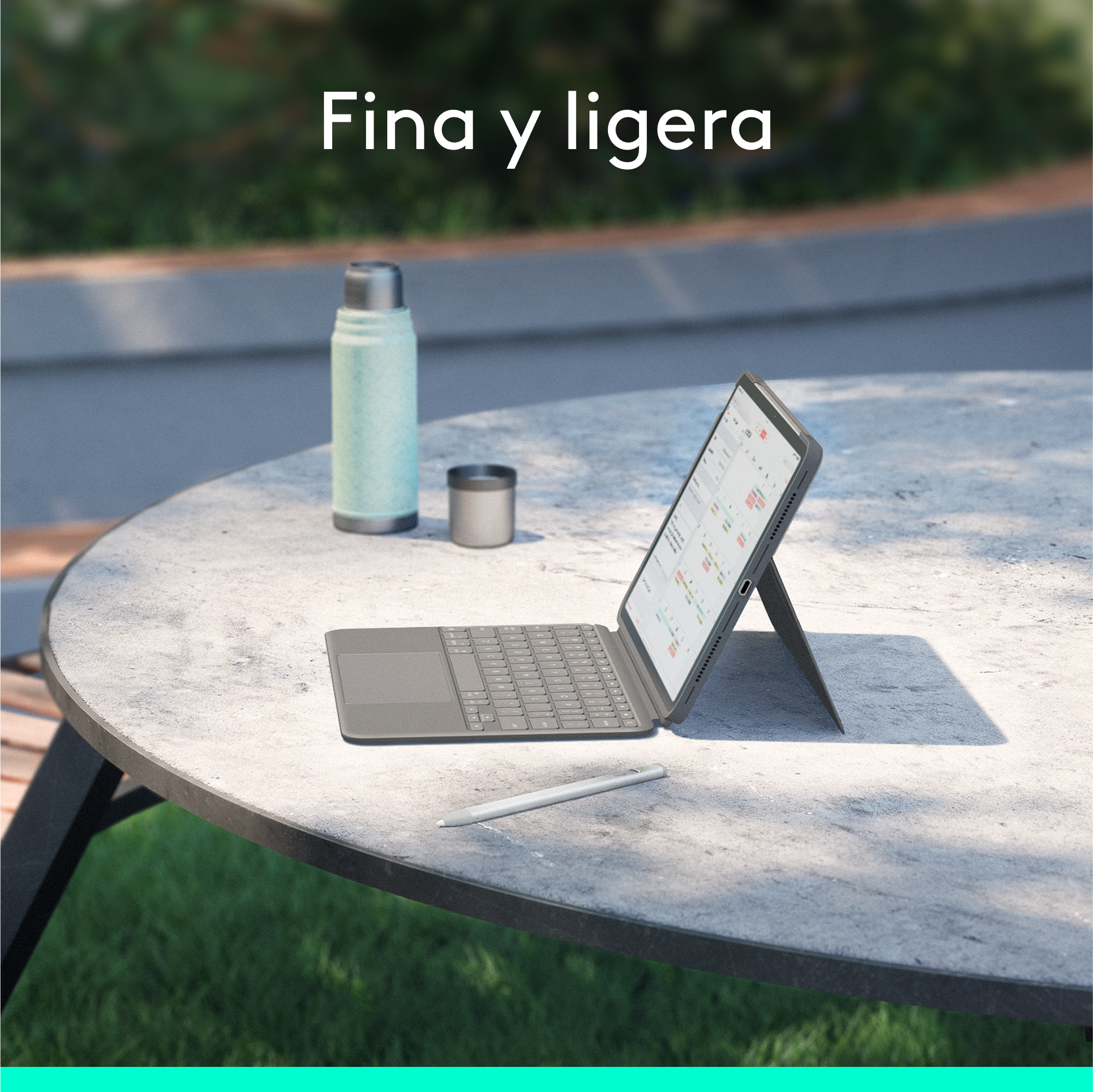 Tableta con teclado sobre una mesa. Junto a una botella y una taza. Campo verde al fondo.