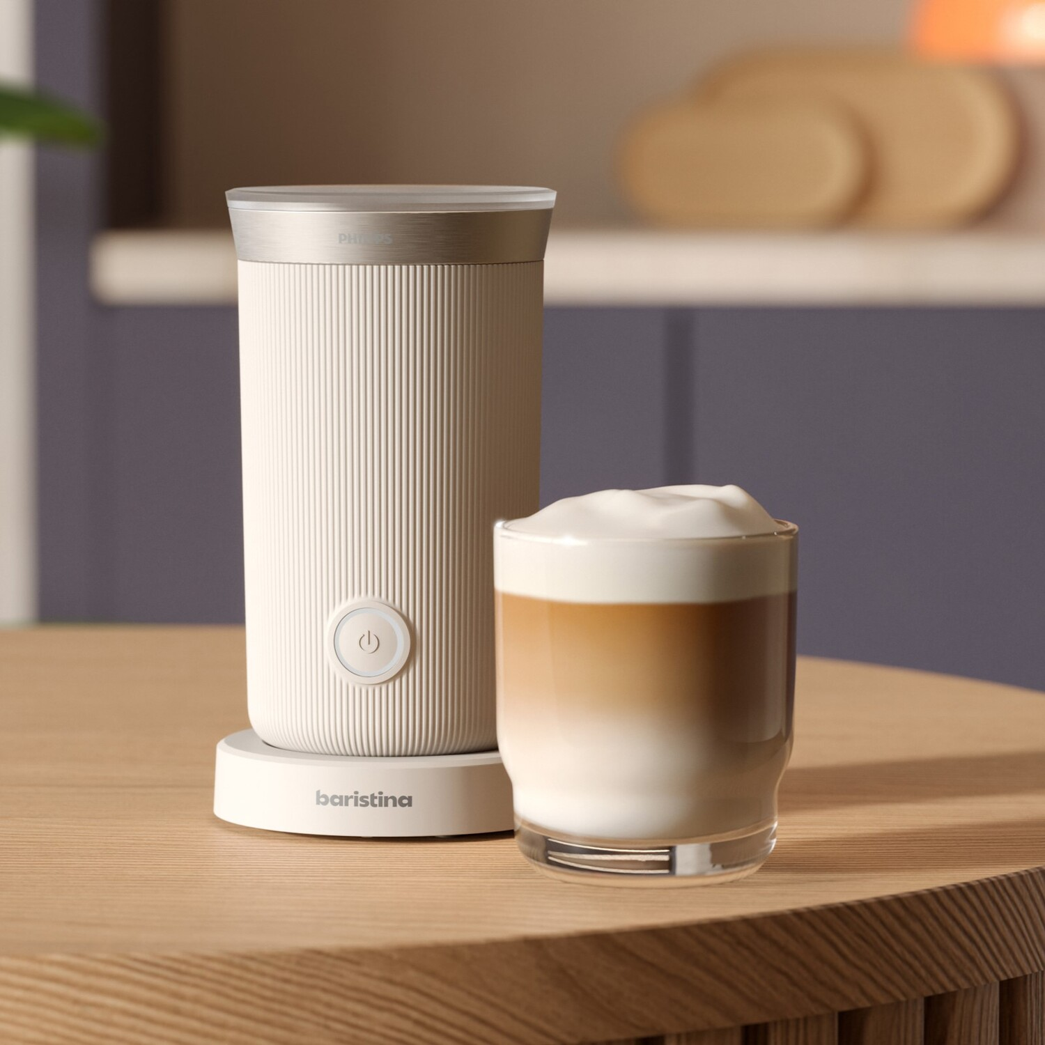 Witte melkopschuimer naast een glas latte. Opschuimer heeft een witte basis en een zilveren bovenkant.