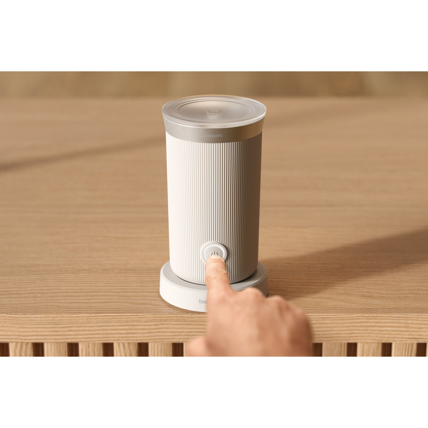 Een vinger drukt op de aan/uit-knop van een klein wit Philips-apparaat.