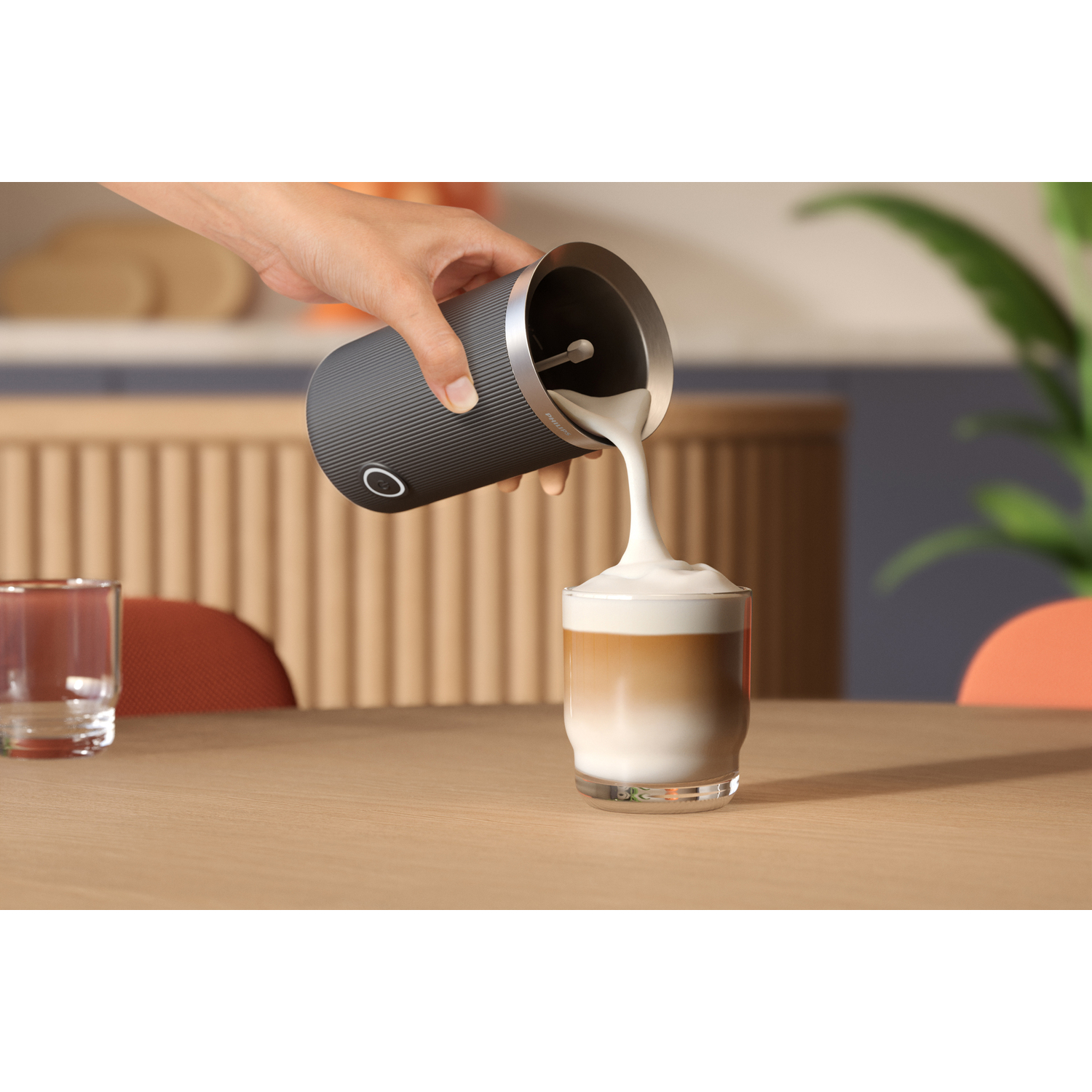 Hand pouring milk foam into a glass of coffee. The scene is indoors on a table.