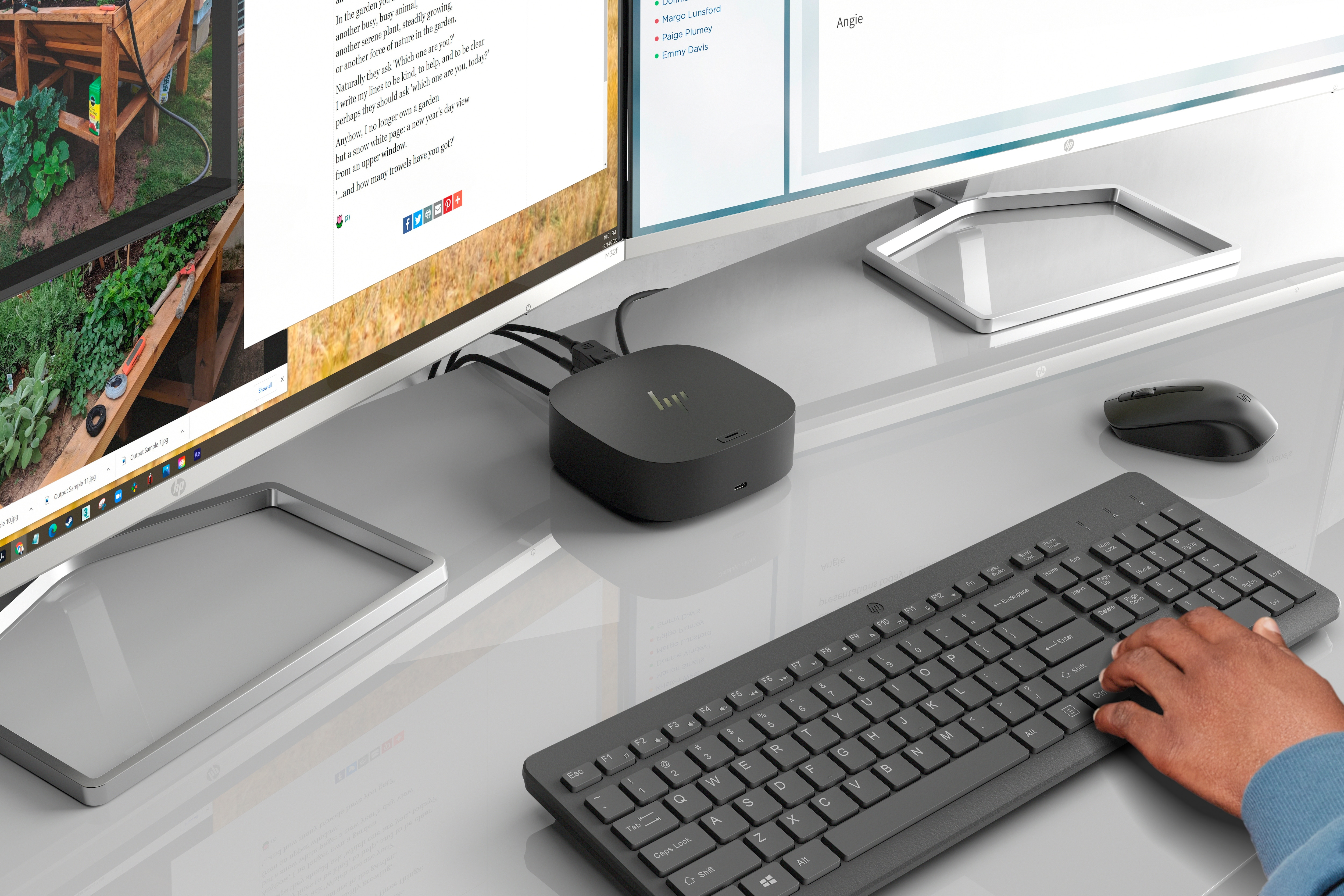 Schreibtisch mit Monitoren, Tastatur und eine Person tippt.