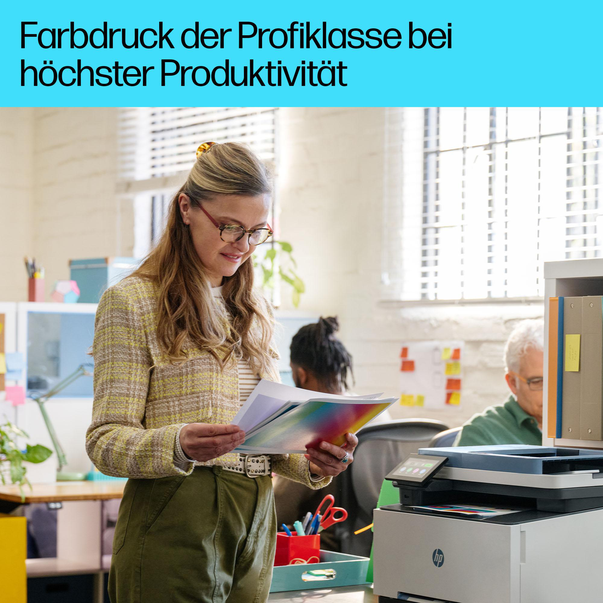 Frau im Büro betrachtet Farbmuster, Drucker und Kollegen im Hintergrund.