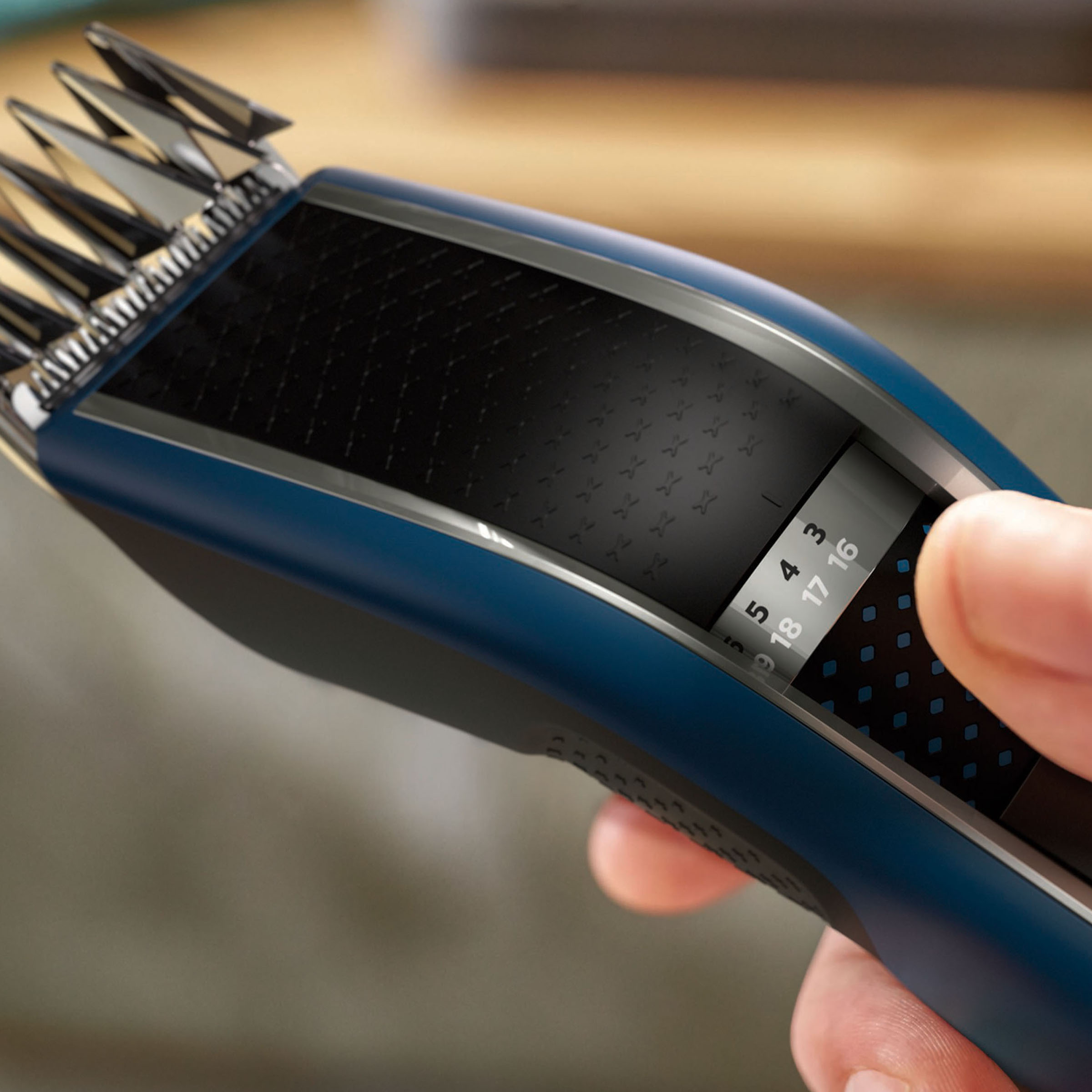 Dłoń trzymająca niebiesko-czarną maszynkę do strzyżenia włosów ze skalą numerów.