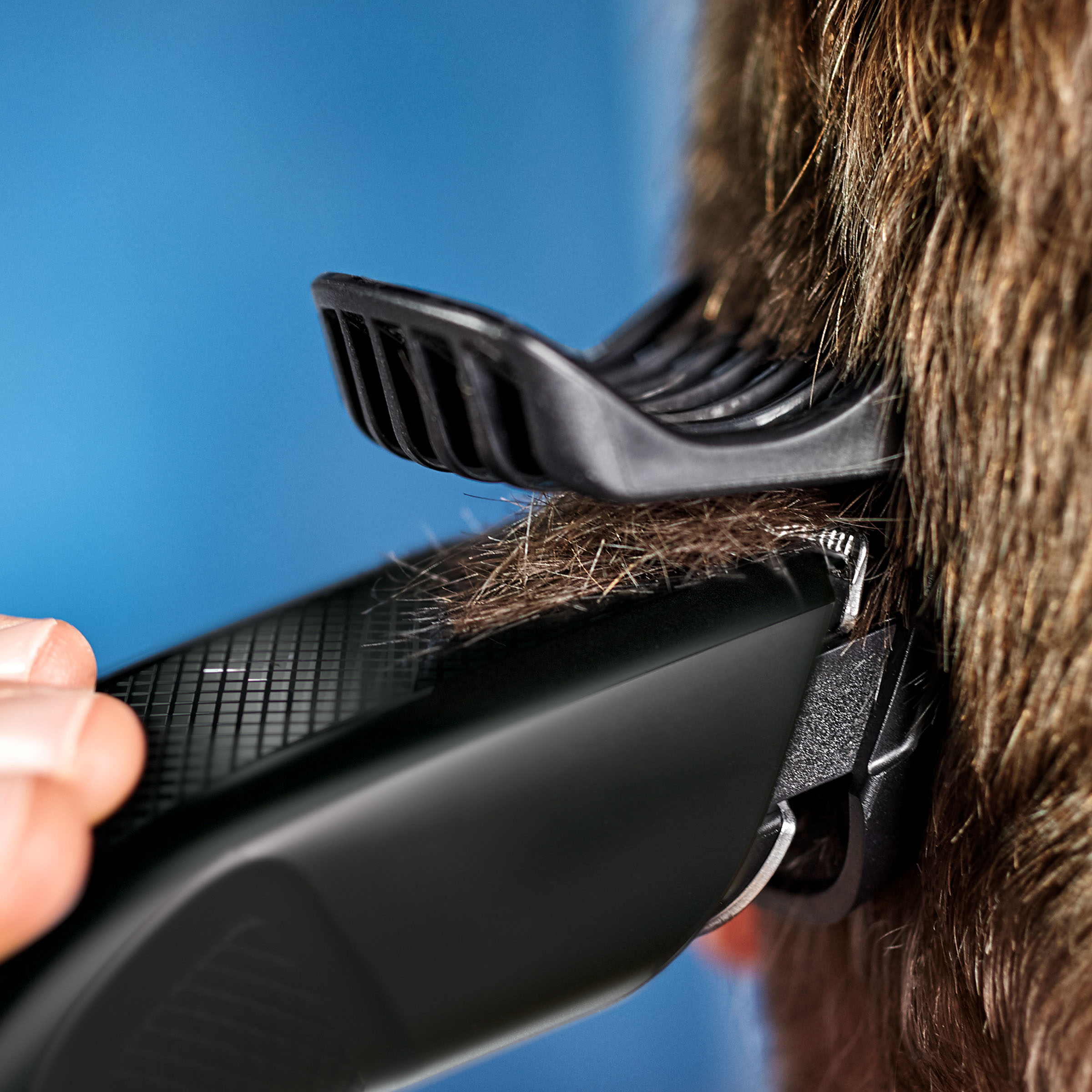 Czyjeś włosy są strzyżone czarną maszynką. Maszynka ma założoną nasadkę.