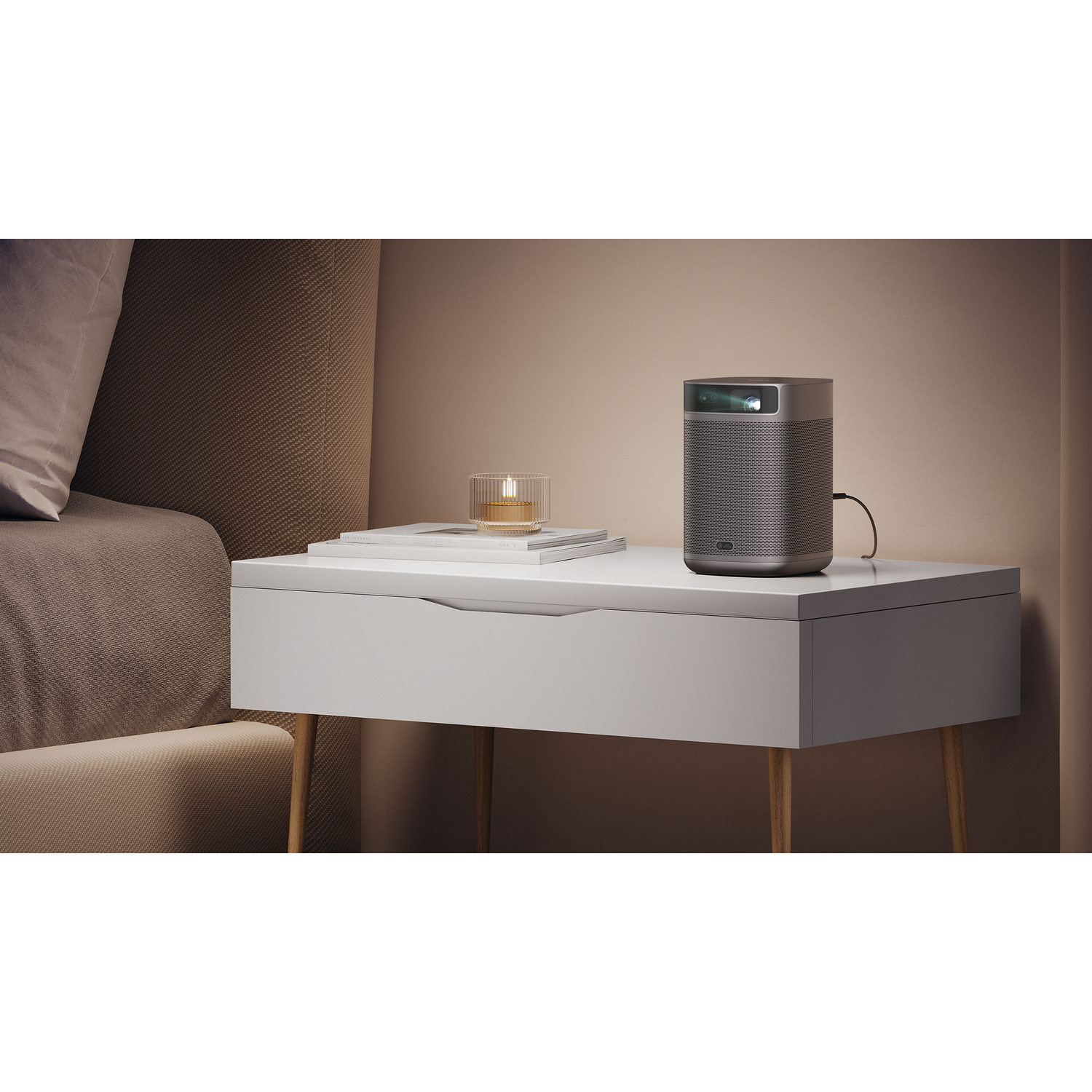A gray cylindrical projector on a white nightstand. A candle and books are also on the stand.