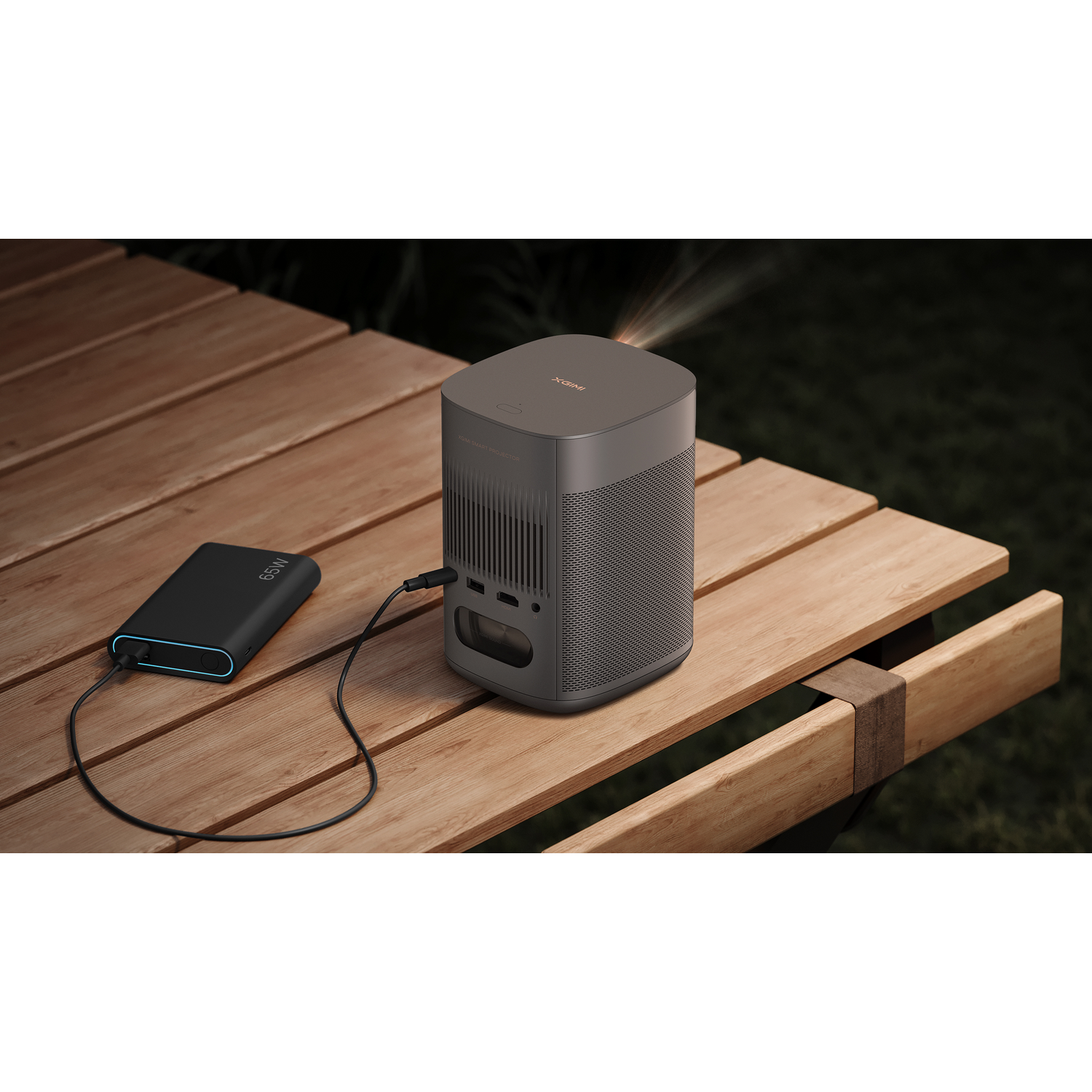 A dark gray projector on a wooden table, connected to a black power bank.