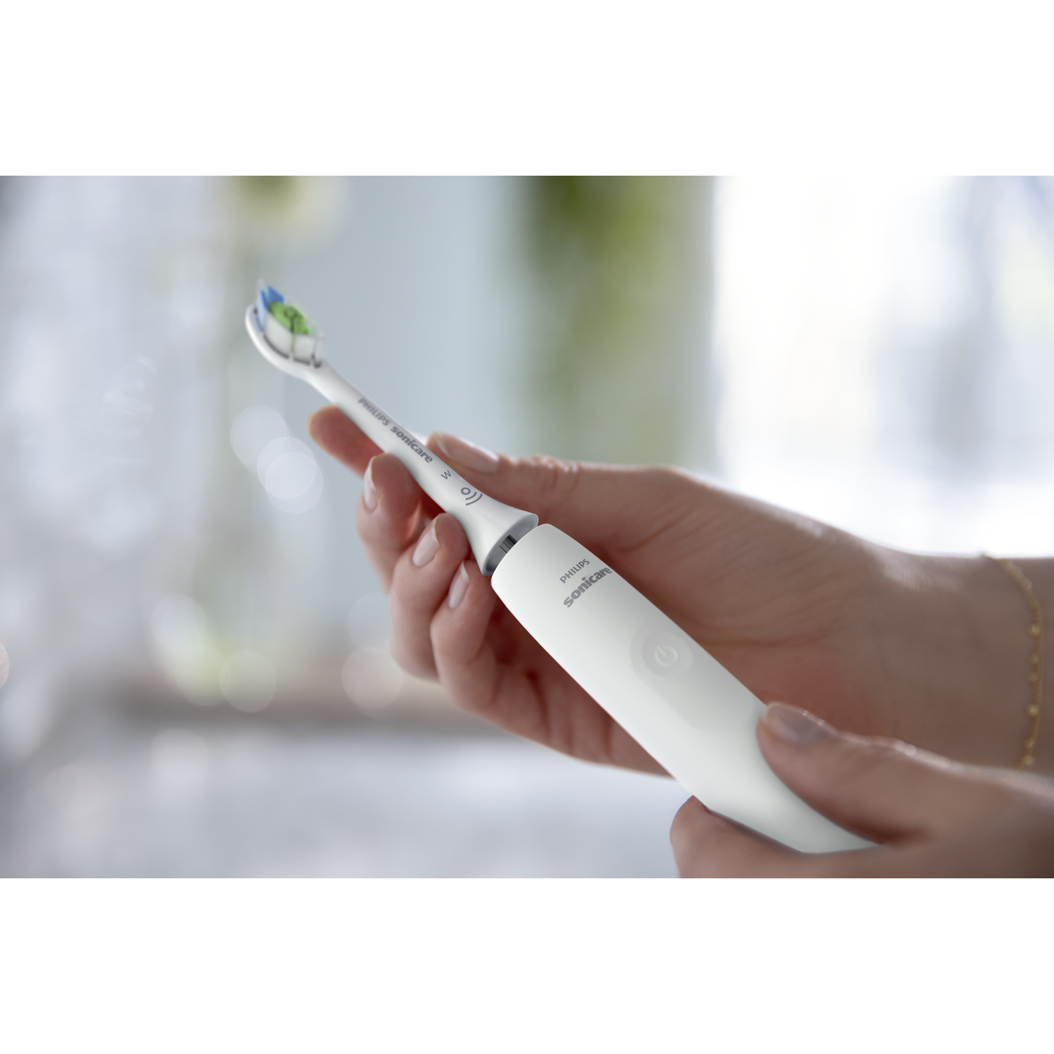 A hand holding a white Philips Sonicare toothbrush, with a blue and green brush head.