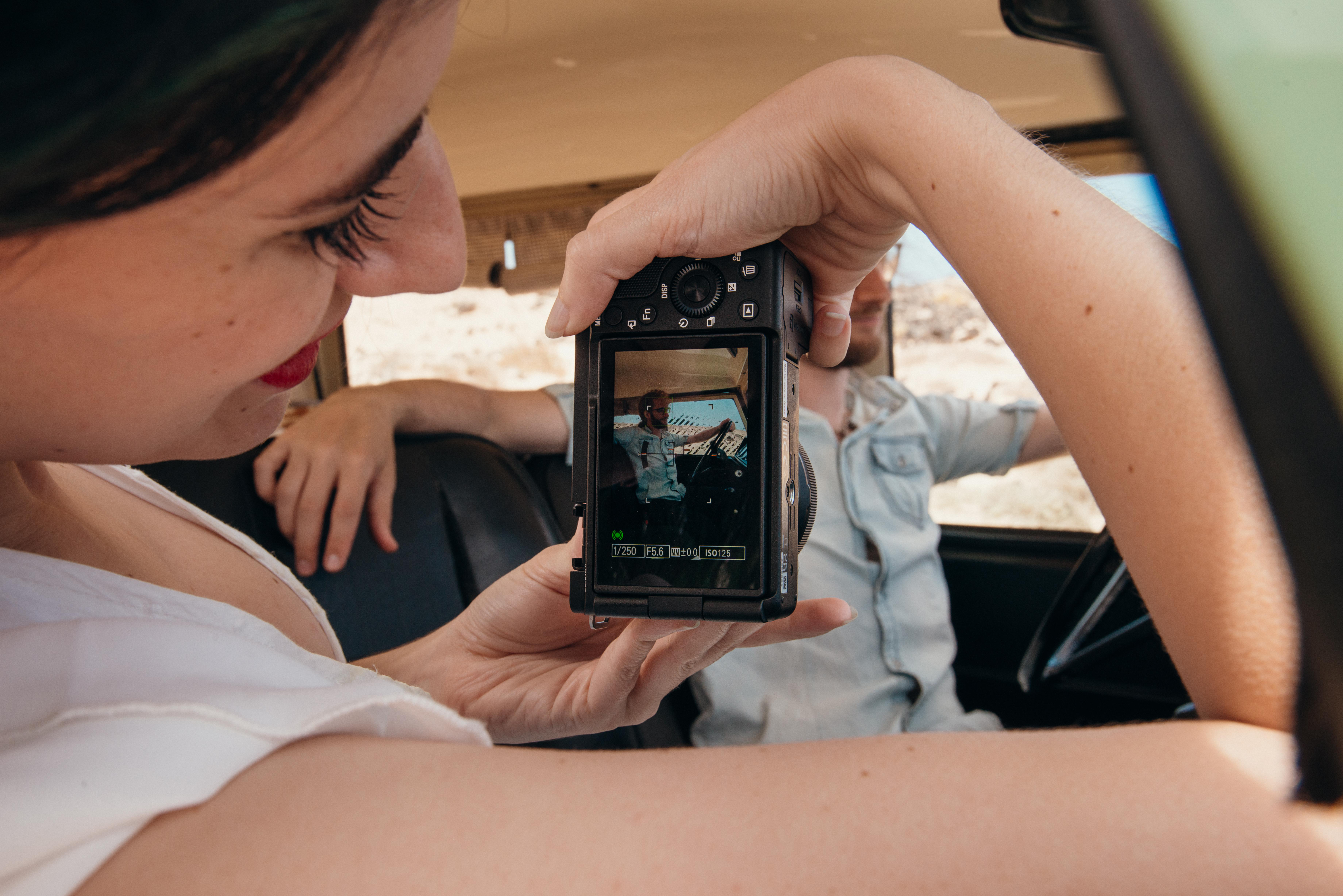 Frau macht Foto von Mann im Auto durch Kamera. Ein Mann sitzt auf dem Fahrersitz.