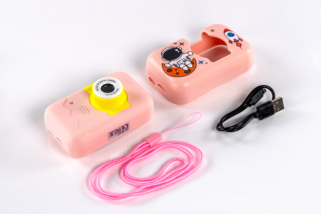 Roket kılıfı, kayış ve USB kablosu ile pembe oyuncak kamera, beyaz zemin üzerinde.
