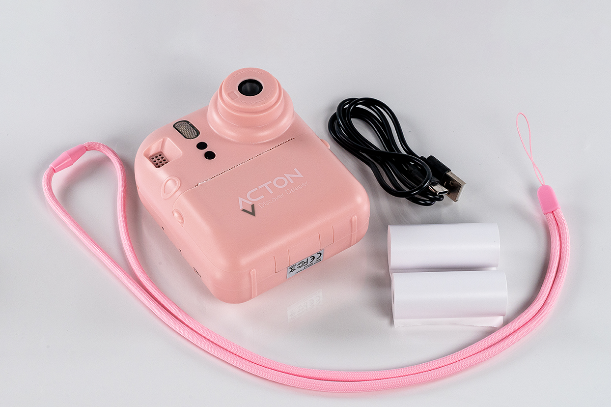 Pembe anında fotoğraf makinesi ve aksesuarları: pembe kayış, siyah kablo ve iki film rulosu.