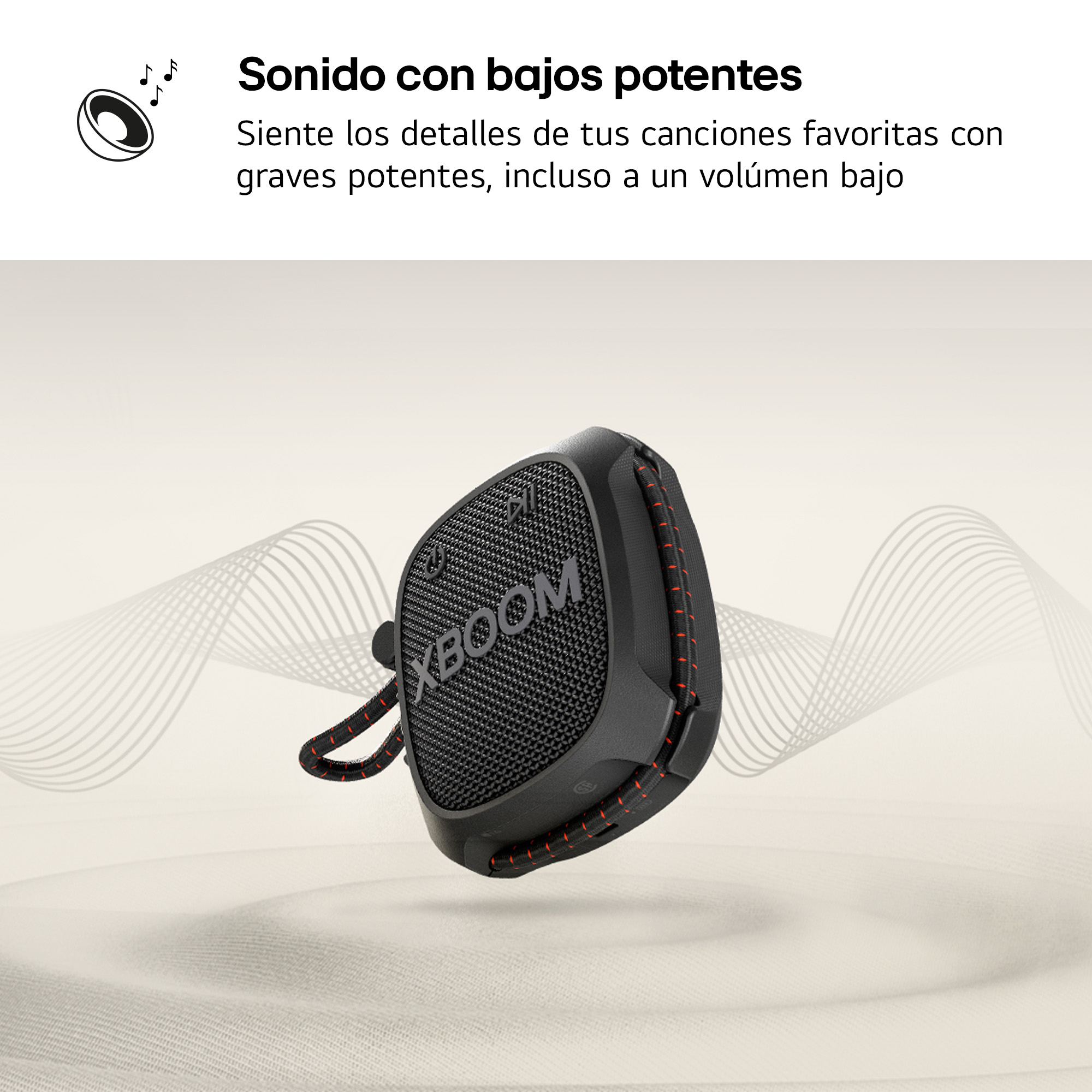 Altavoz negro con frontal de malla, detalles rojos y cordón, sobre fondo arenoso.