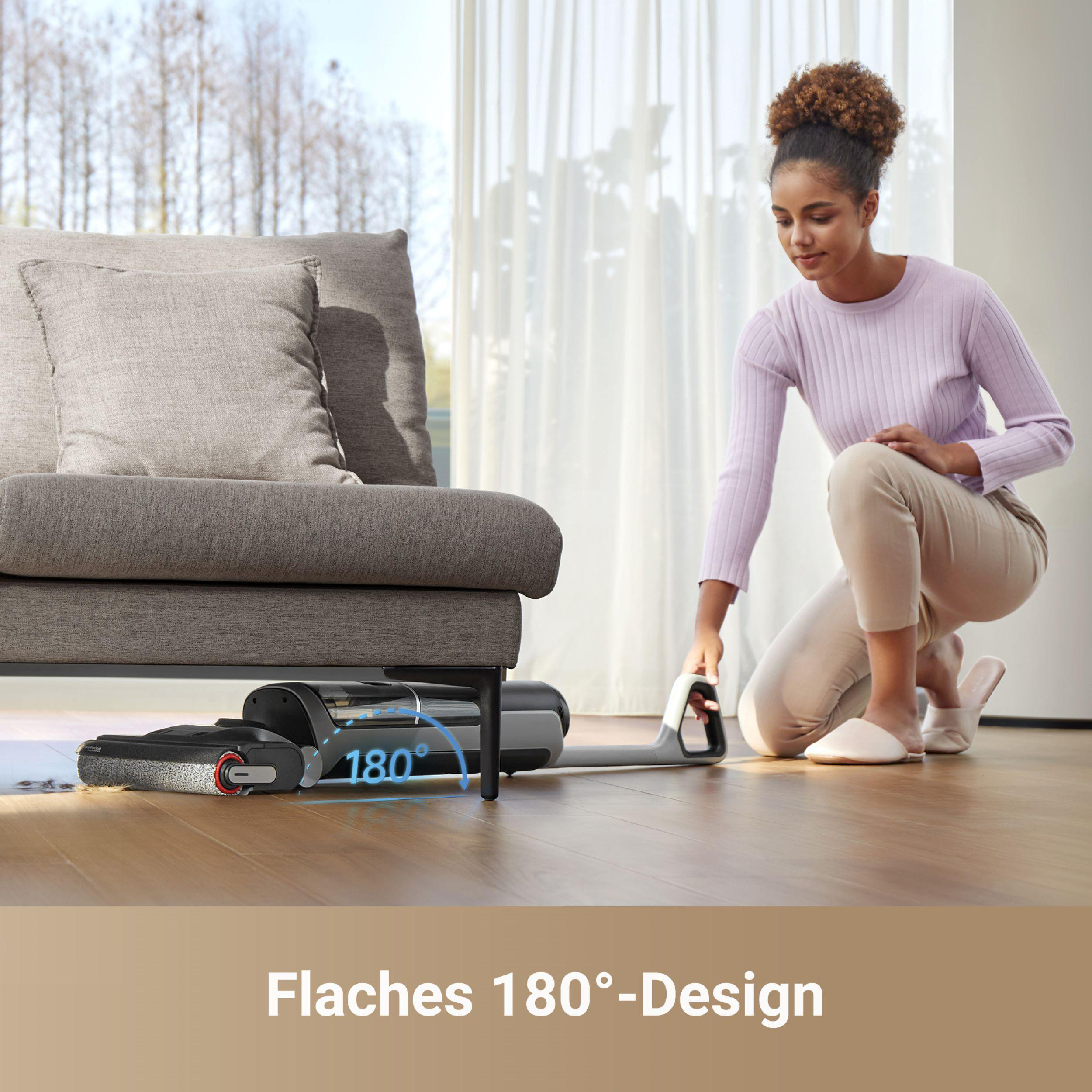 Frau reinigt Boden mit Staubsauger nahe dem Sofa.