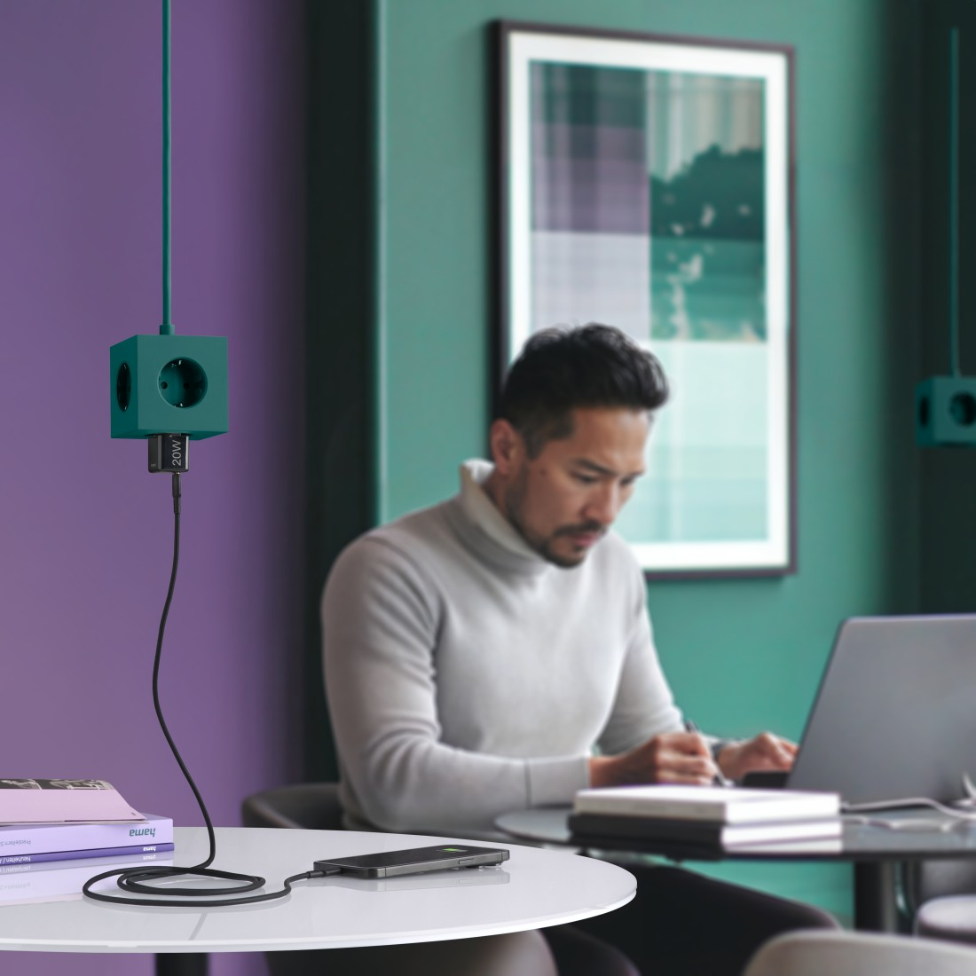 Mann arbeitet an einem Schreibtisch, grüne Steckdosenleiste mit schwarzem Kabel, Telefon lädt.