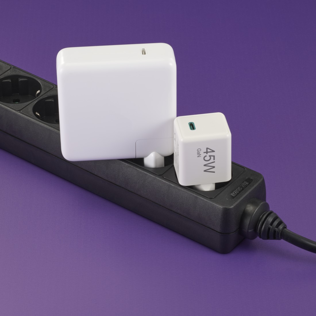 Zwei weiße Netzadapter, die in eine schwarze Steckdosenleiste vor violettem Hintergrund eingesteckt sind.