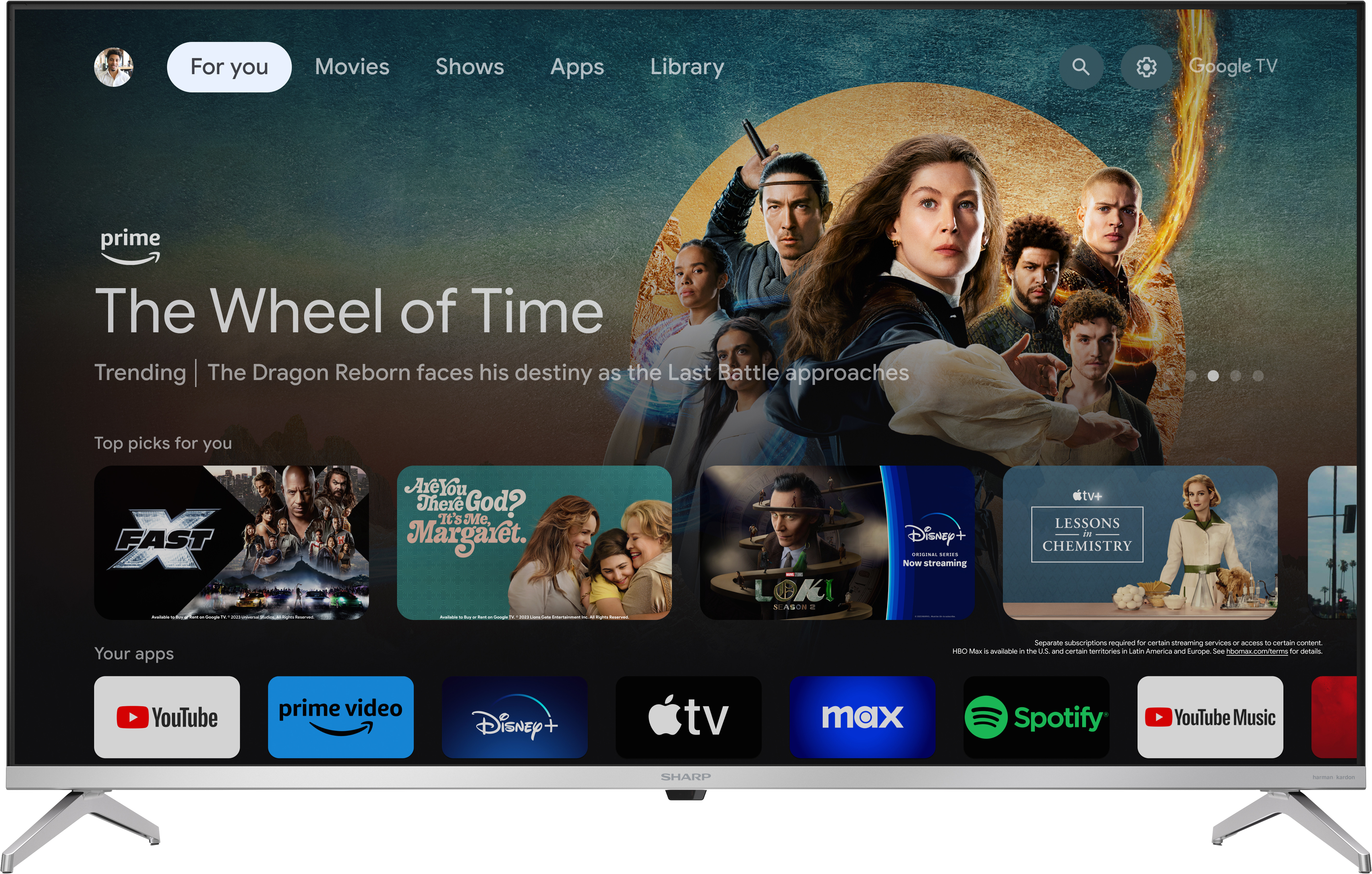 Egy Sharp TV, amely egy Google TV felületet jelenít meg film-bélyegképekkel. A TV egy ezüst talapzaton áll.