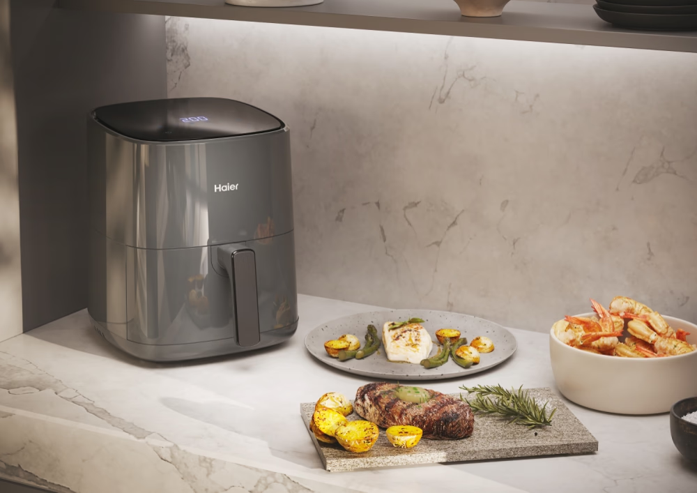 Une friteuse à air avec de la nourriture sur un comptoir. Steak, crevettes et pommes de terre sont visibles.