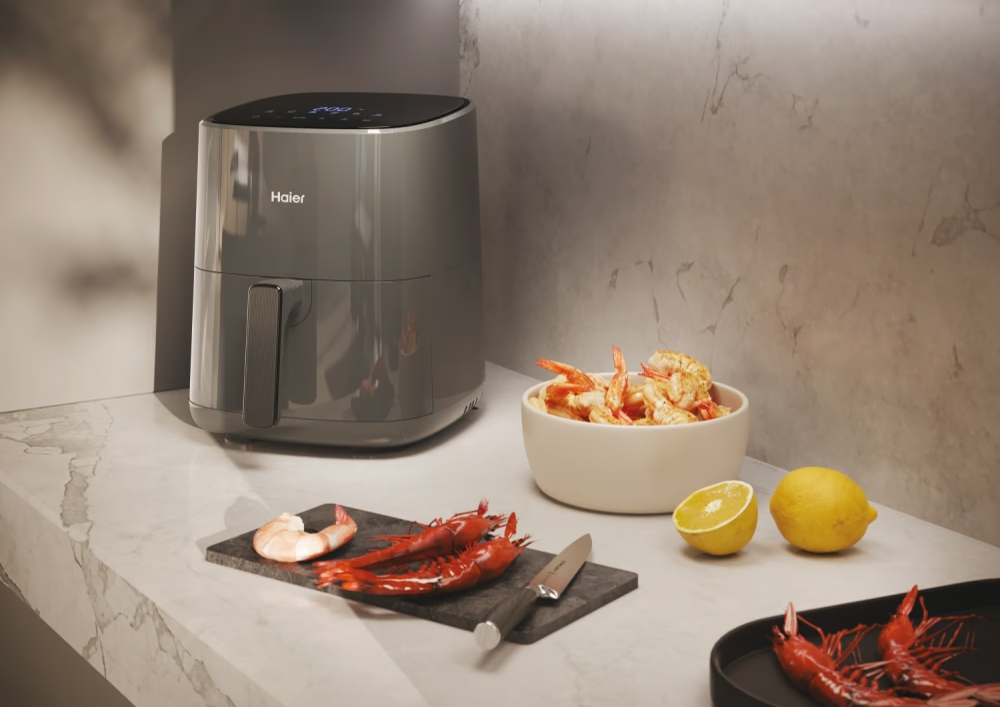 Friteuse à air avec de la nourriture sur un comptoir. Crevettes, citrons et un couteau sont visibles.
