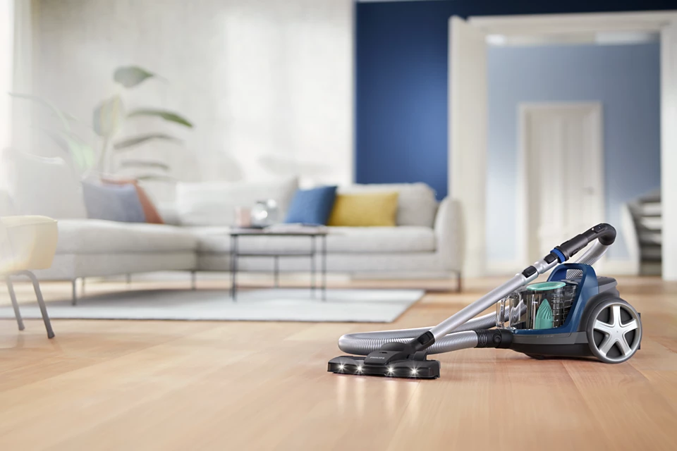 Ein Staubsauger auf einem Holzboden in einem Wohnzimmer mit Sofa und Tür.