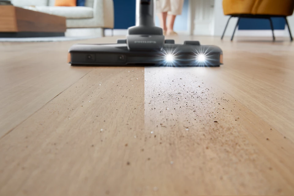 Ein Staubsauger reinigt einen Holzboden. Die Hälfte des Bodens ist sauber, die andere Hälfte schmutzig.
