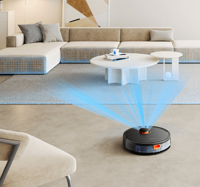 Czarny odkurzacz robot na jasnoszarej podłodze. Meble: sofa, stół i krzesło.