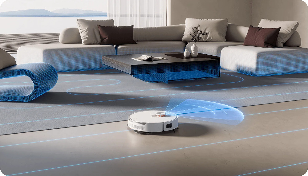 Biały odkurzacz robot na szarym dywanie. W tle sofa i stolik kawowy.