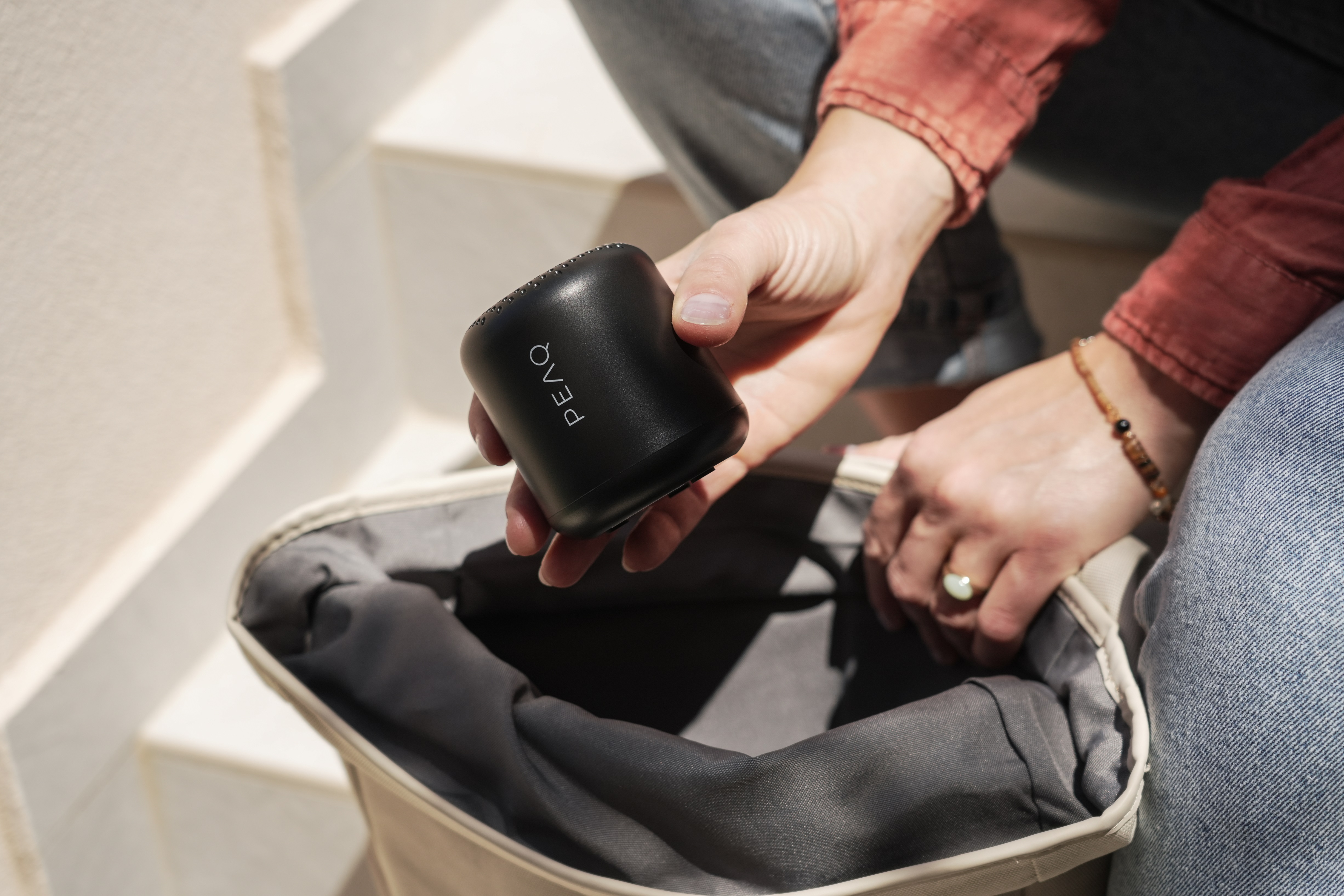 Ręce osoby trzymającej mały czarny walec, w pobliżu beżowej torby.