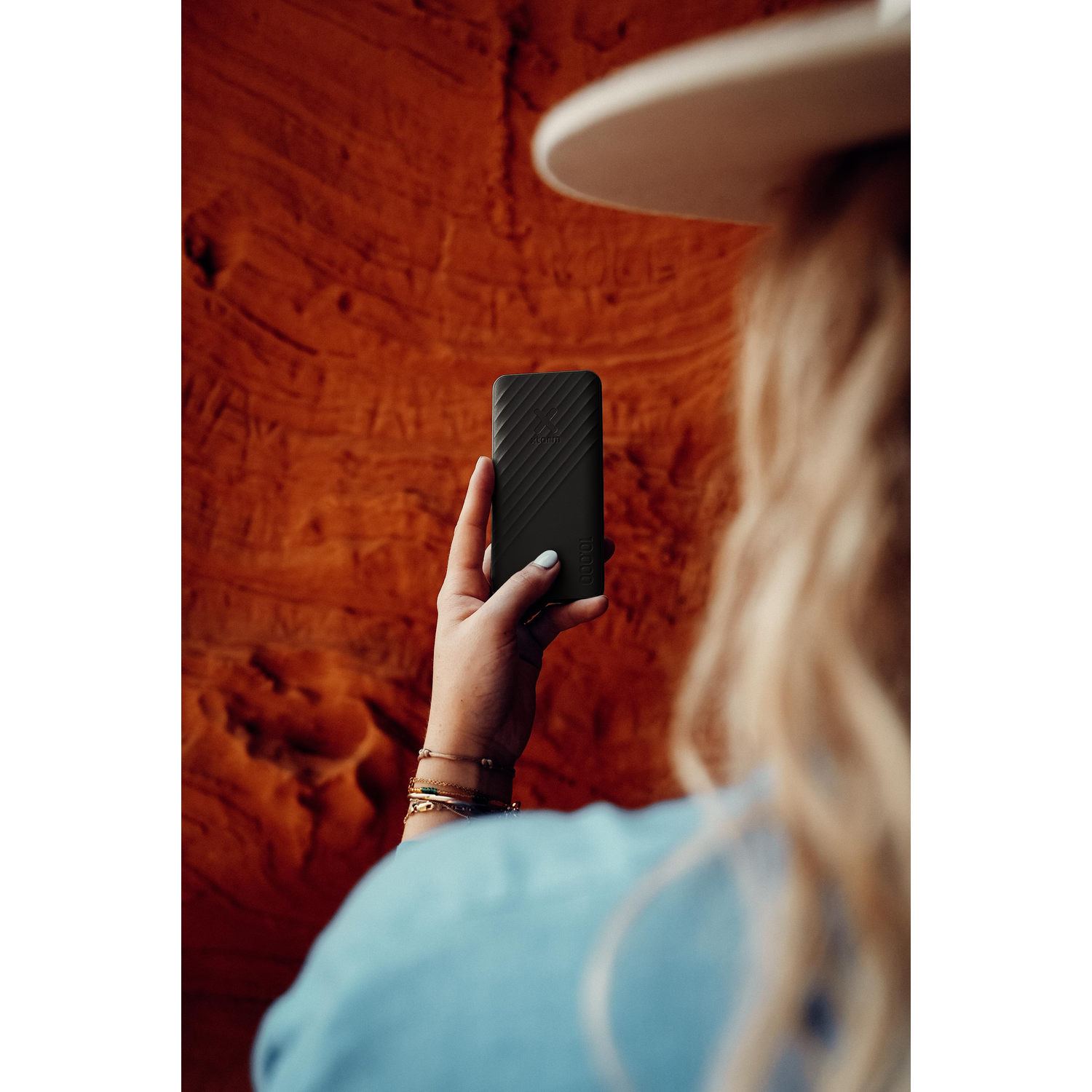 A woman holding a black portable hard drive in front of a red rock formation.