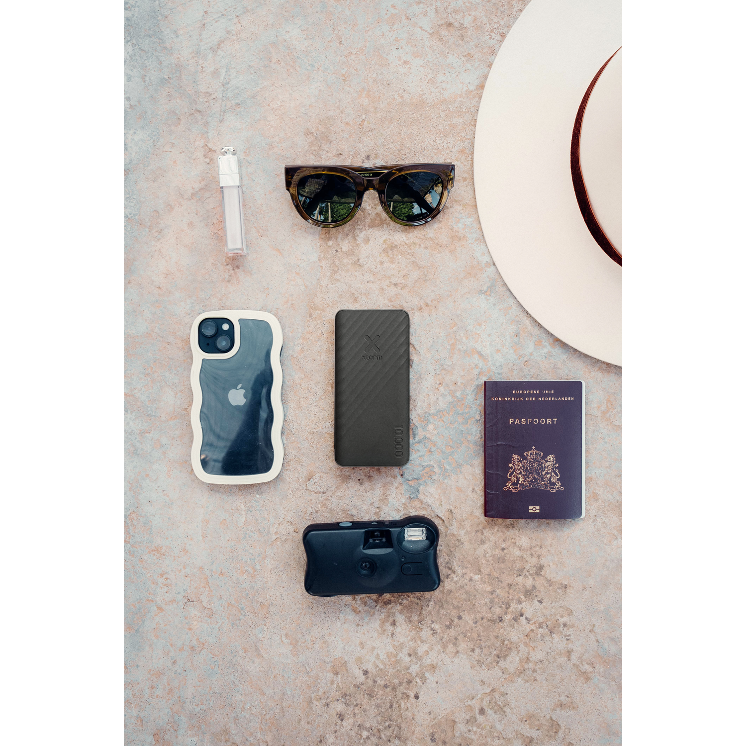 Sunglasses, passport, phone, power bank, camera, and hat are arranged on a surface.
