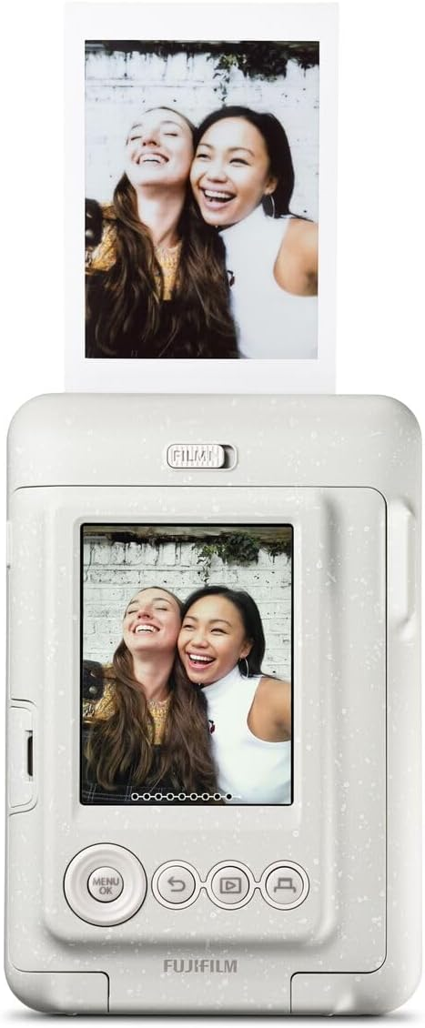 Dos mujeres sonriendo, sosteniendo una foto de una cámara instantánea. La cámara es blanca con motas.