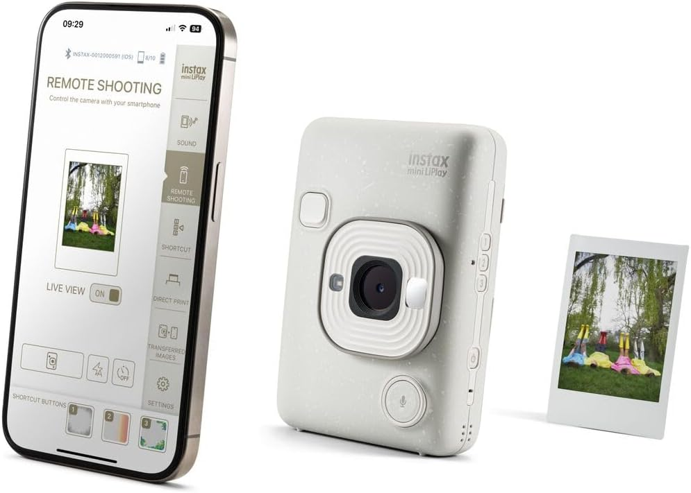 Teléfono con app de cámara, cámara Instax y foto impresa, todo sobre superficie blanca.