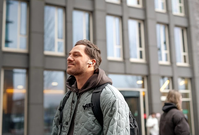 Mężczyzna noszący słuchawki na zewnątrz, z budynkiem w tle.
