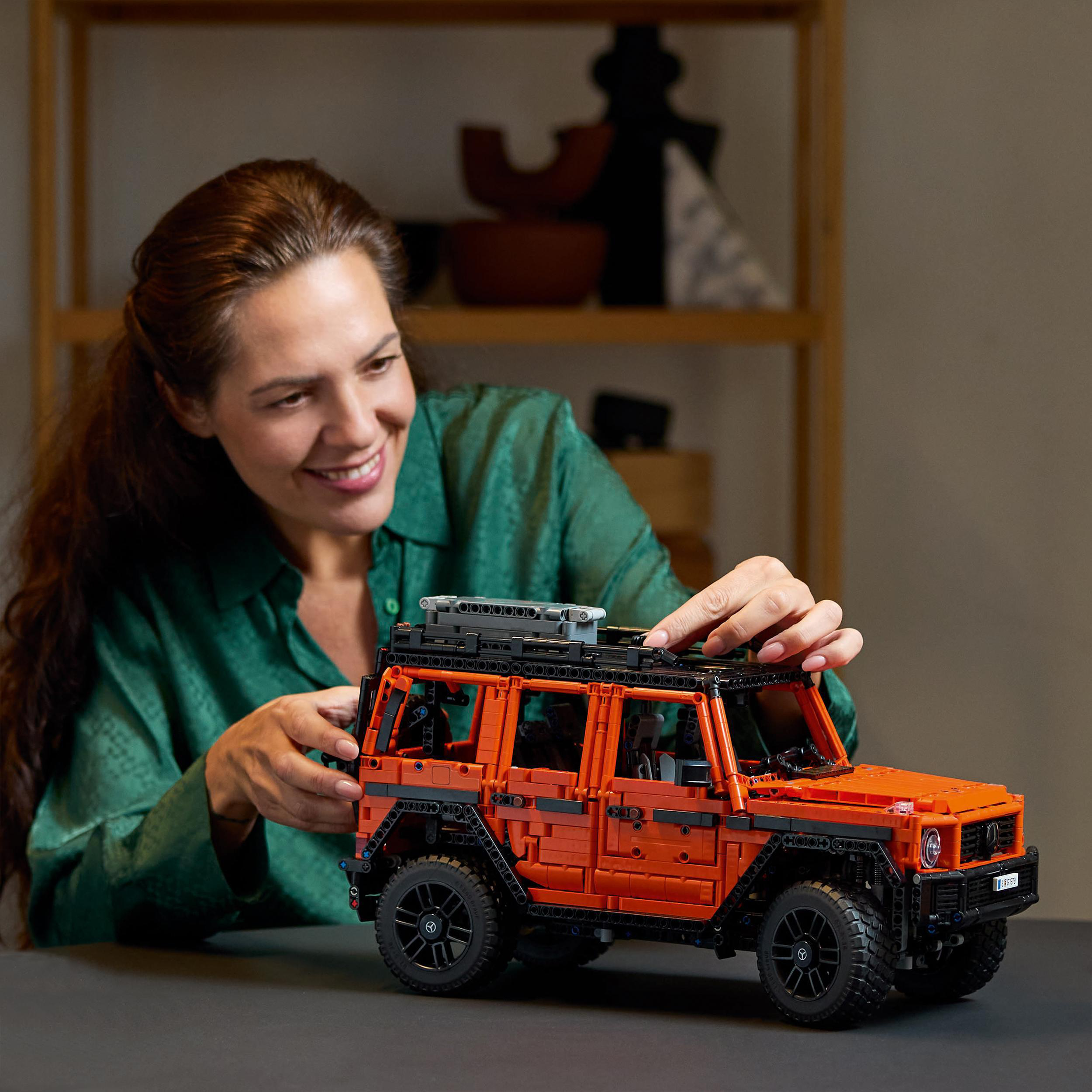 Frau baut ein orangefarbenes LEGO-Auto. Sie lächelt. Das Auto steht auf einem schwarzen Tisch.
