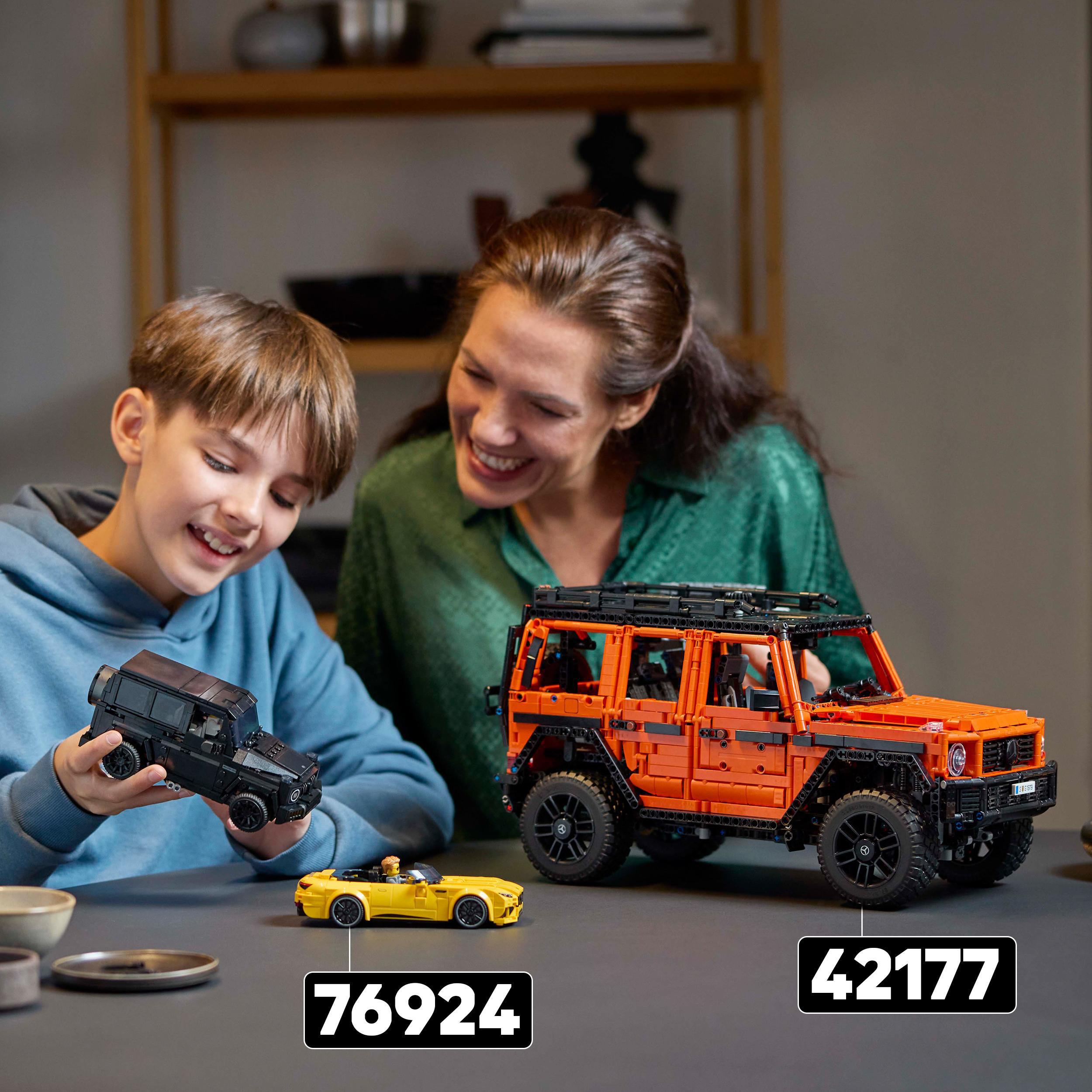 Ein Junge und eine Frau betrachten Lego-Autos, ein orangefarbenes und ein schwarzes Modell.