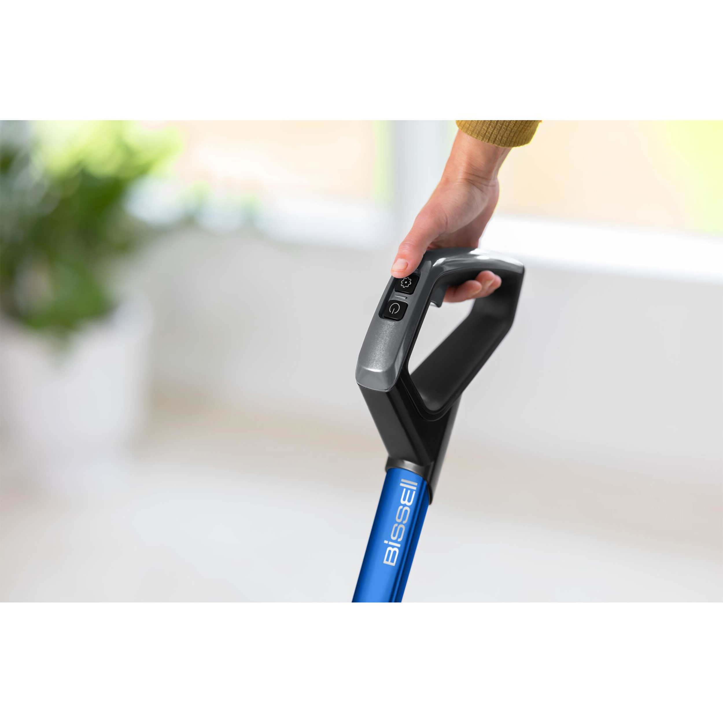 Eine Hand hält einen blauen Bissell-Staubsaugergriff mit Einschaltknöpfen.
