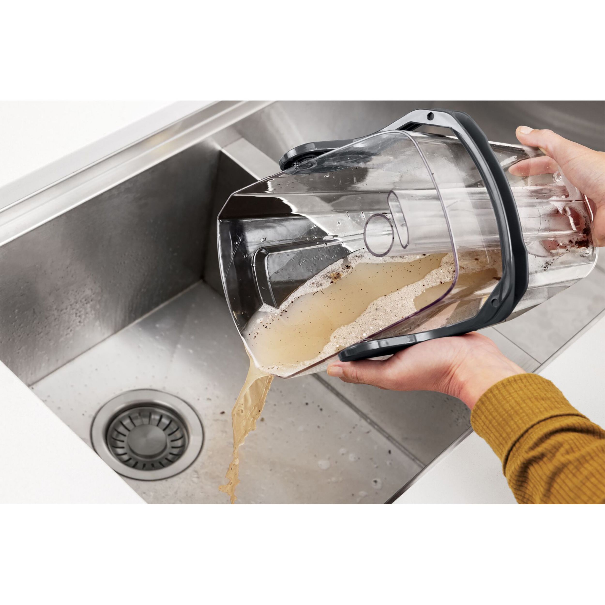 Eine Person gießt schmutziges Wasser aus dem Behälter eines Staubsaugers in ein Waschbecken.
