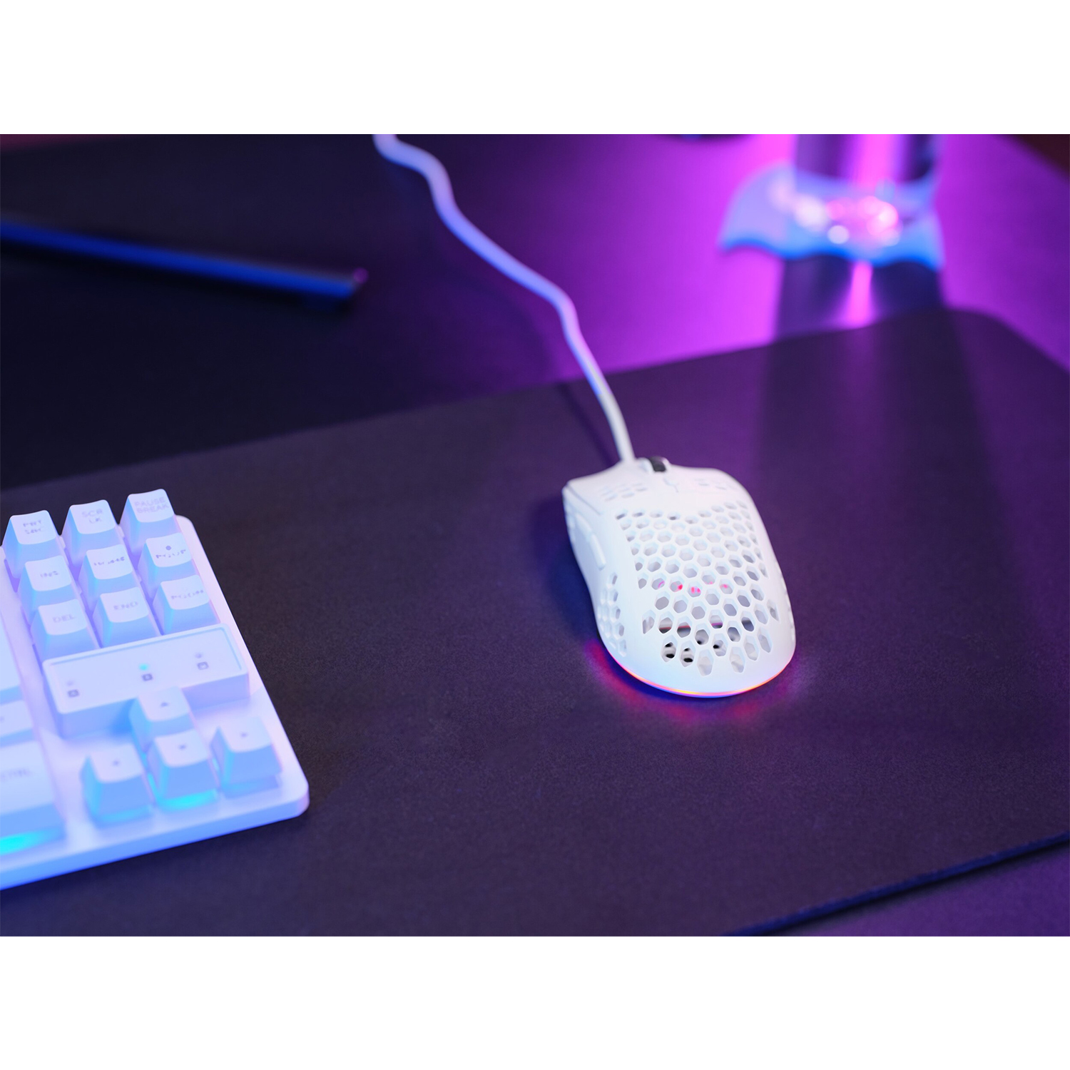 Mouse da gioco bianco su tappetino nero, tastiera a sinistra. Sfondo viola e nero.