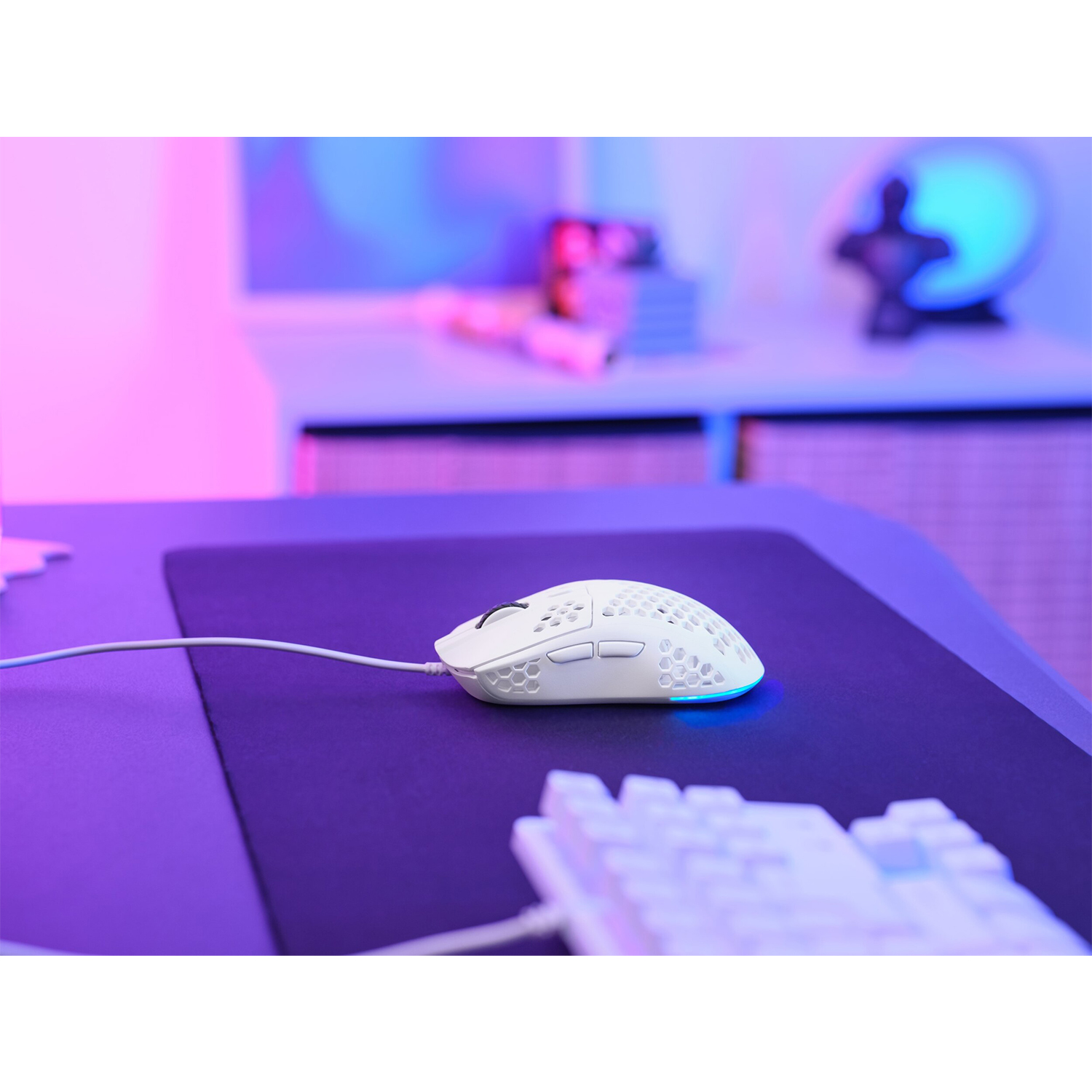 Un mouse da gioco bianco su un tappetino nero, con tastiera in primo piano e illuminazione colorata.