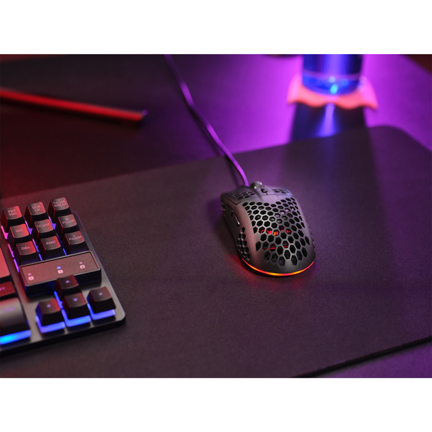 Mouse da gaming nero con design a nido d'ape su un tappetino nero, accanto a una tastiera.