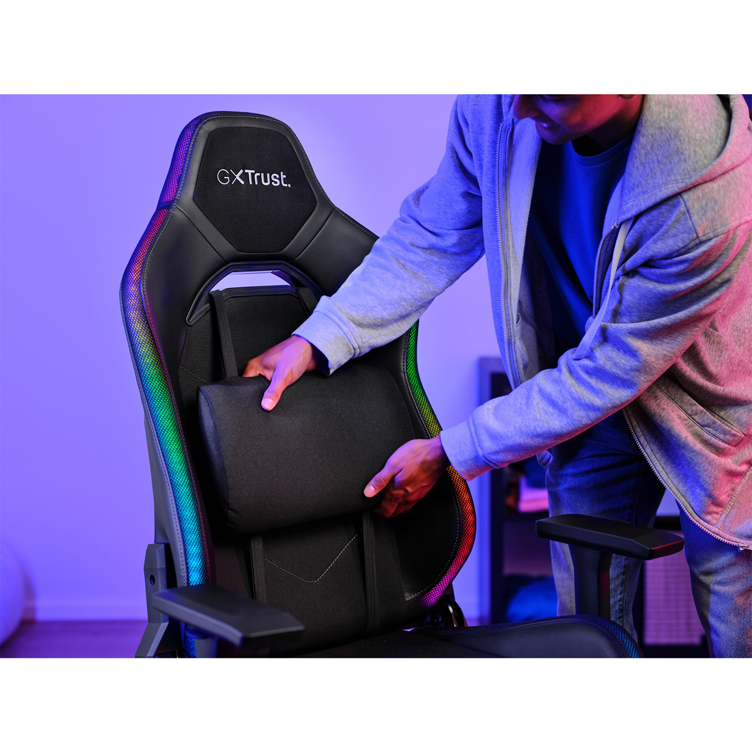Una persona regola il cuscino di supporto lombare di una sedia da gaming GXTrust nera con una striscia luminosa arcobaleno.