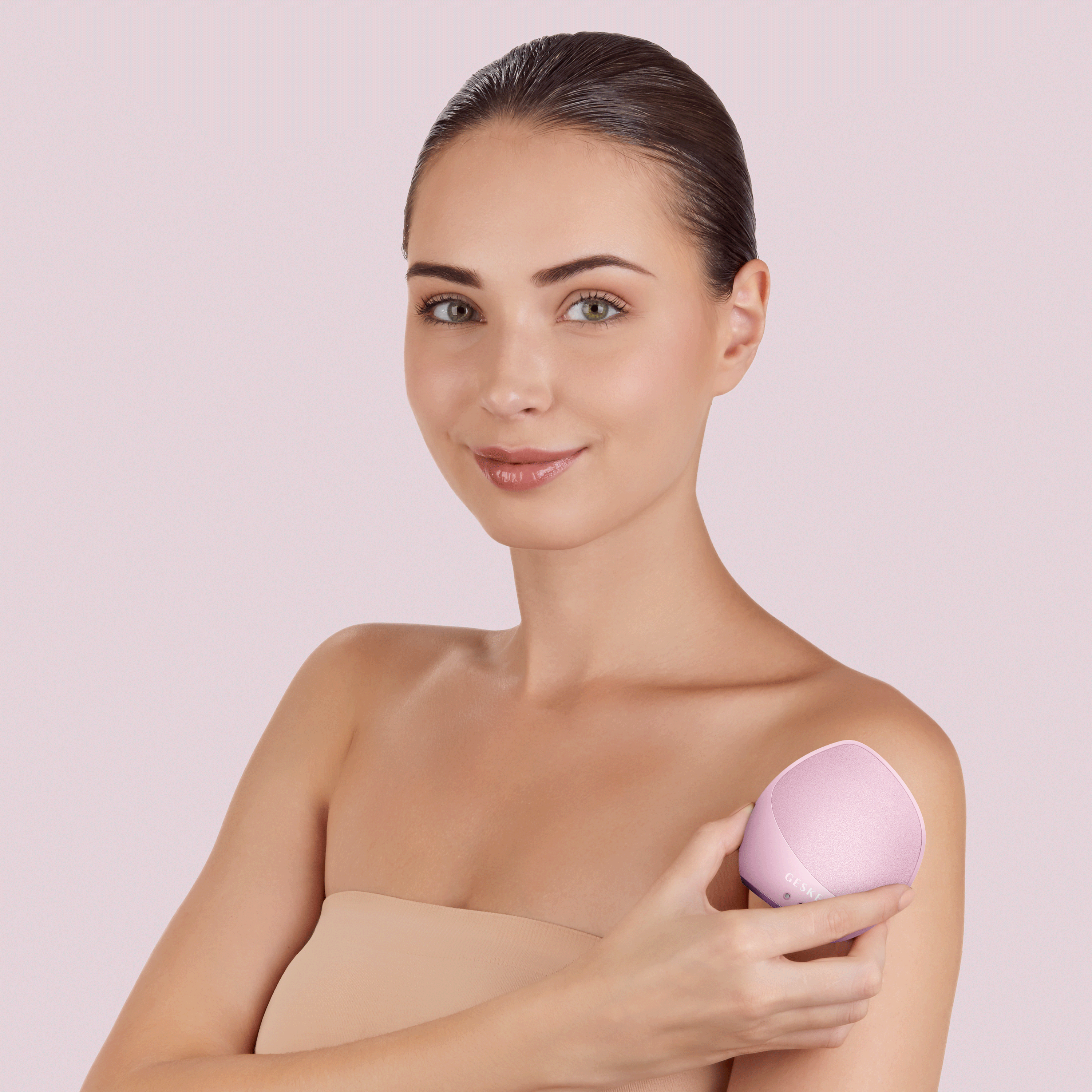 Pembe yüz temizleme cihazı tutan kadın. Açık pembe arka plan.