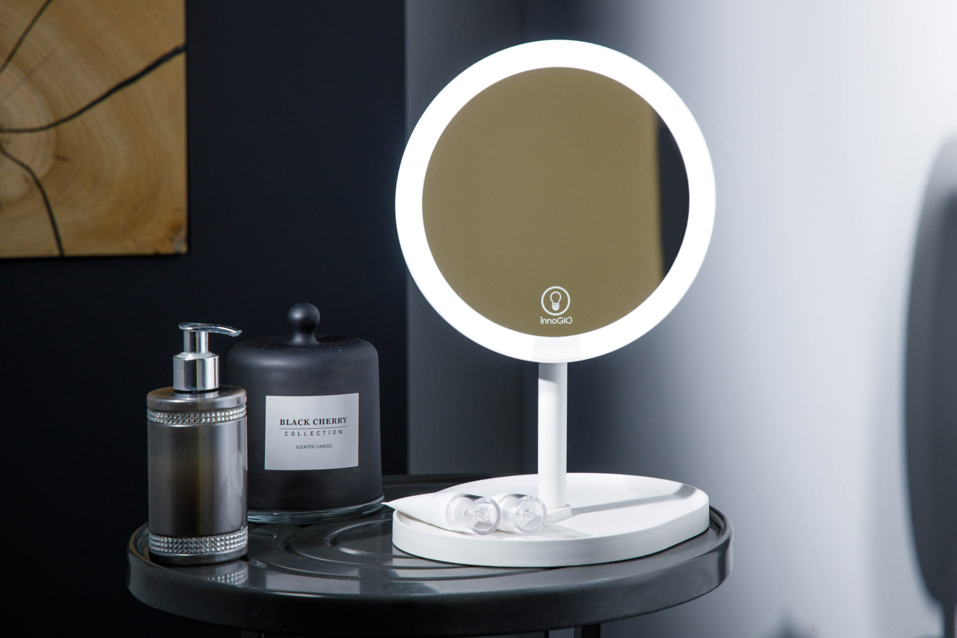 Un espejo de maquillaje blanco con luces, junto a una vela negra y un dispensador de jabón.