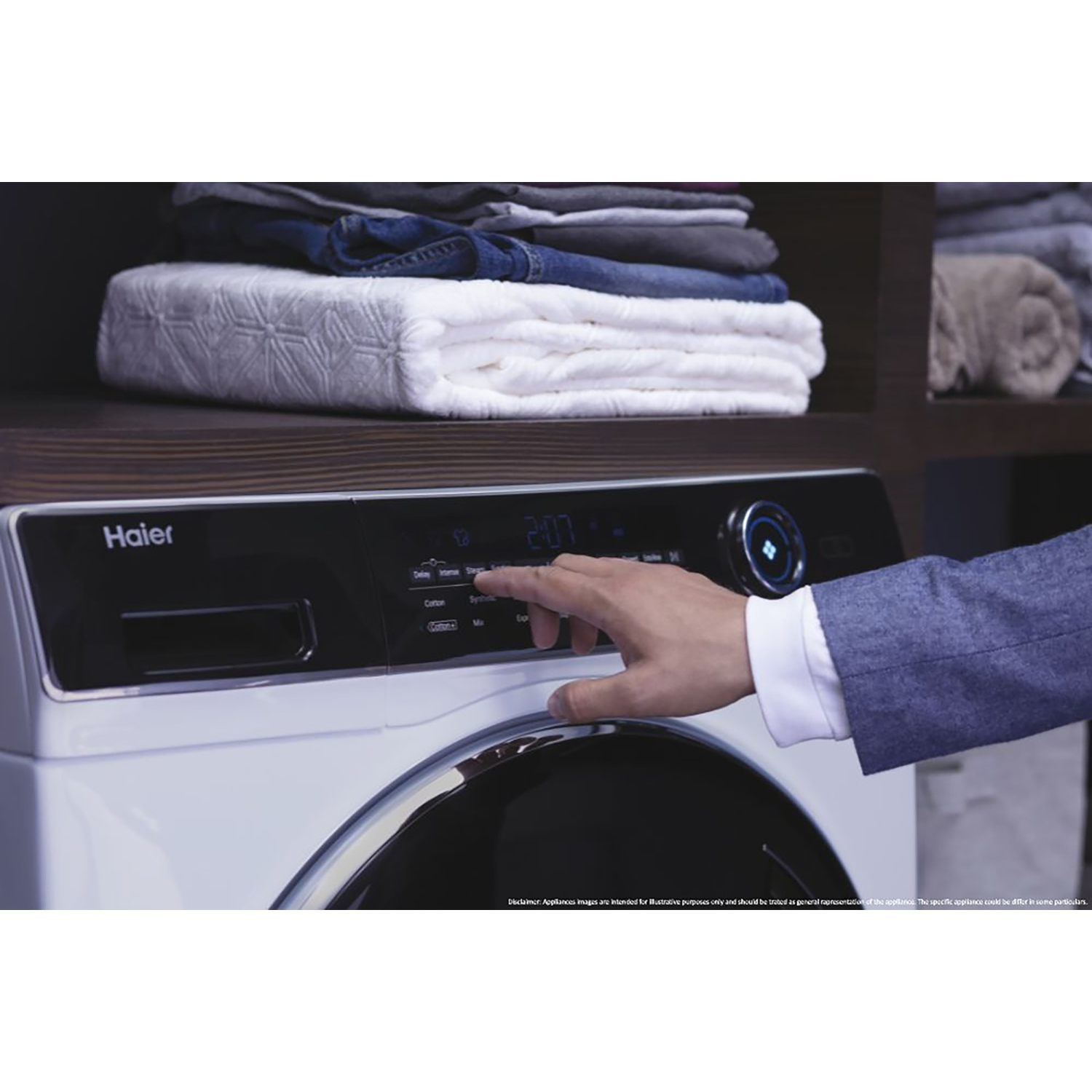Una mano preme un pulsante su una lavatrice Haier bianca, con vestiti impilati sopra.