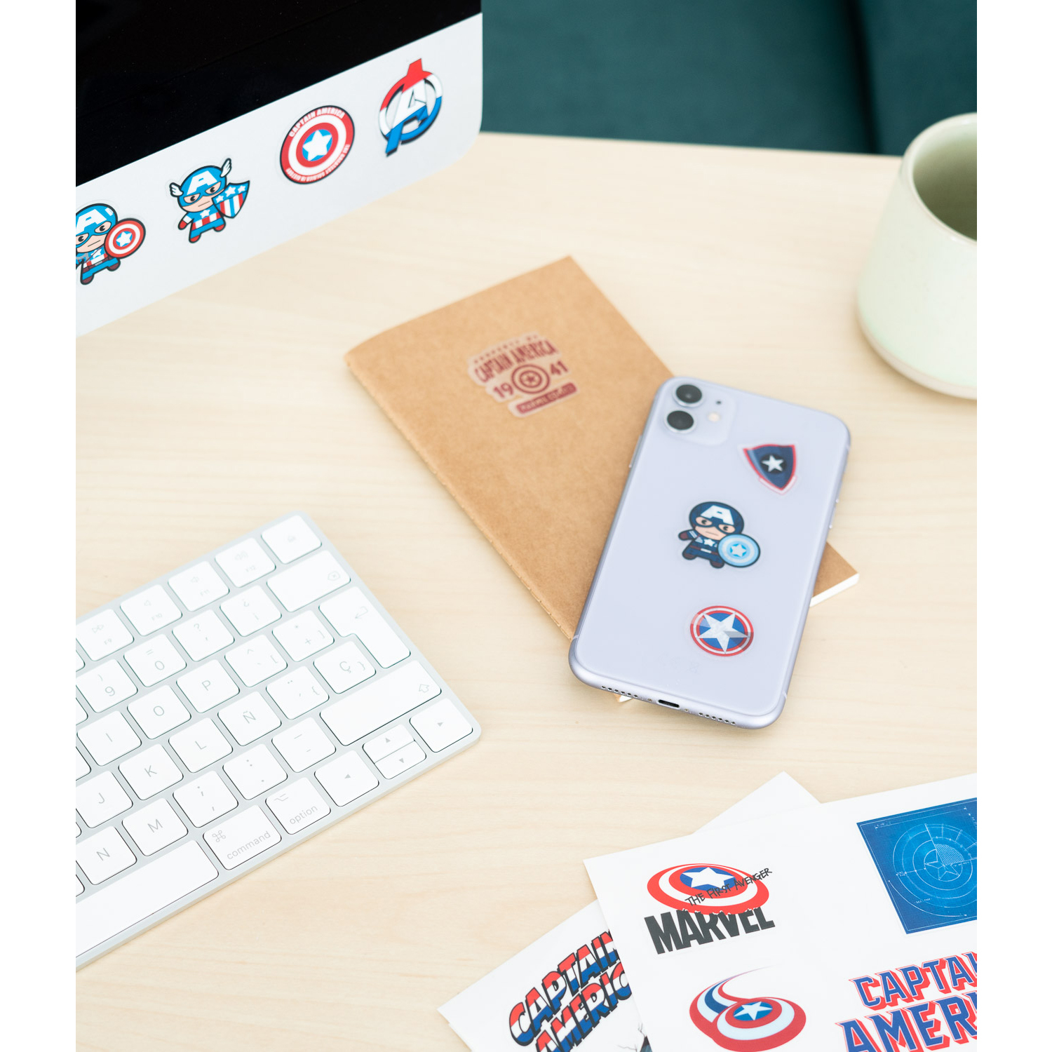Una scrivania con adesivi di Captain America, un quaderno, un telefono e una tastiera.