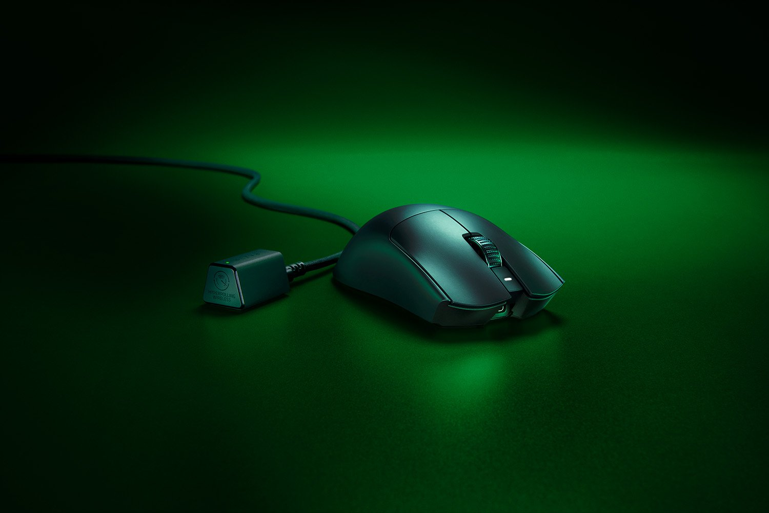 A black gaming mouse with a wired connection and a charging station on a green surface.