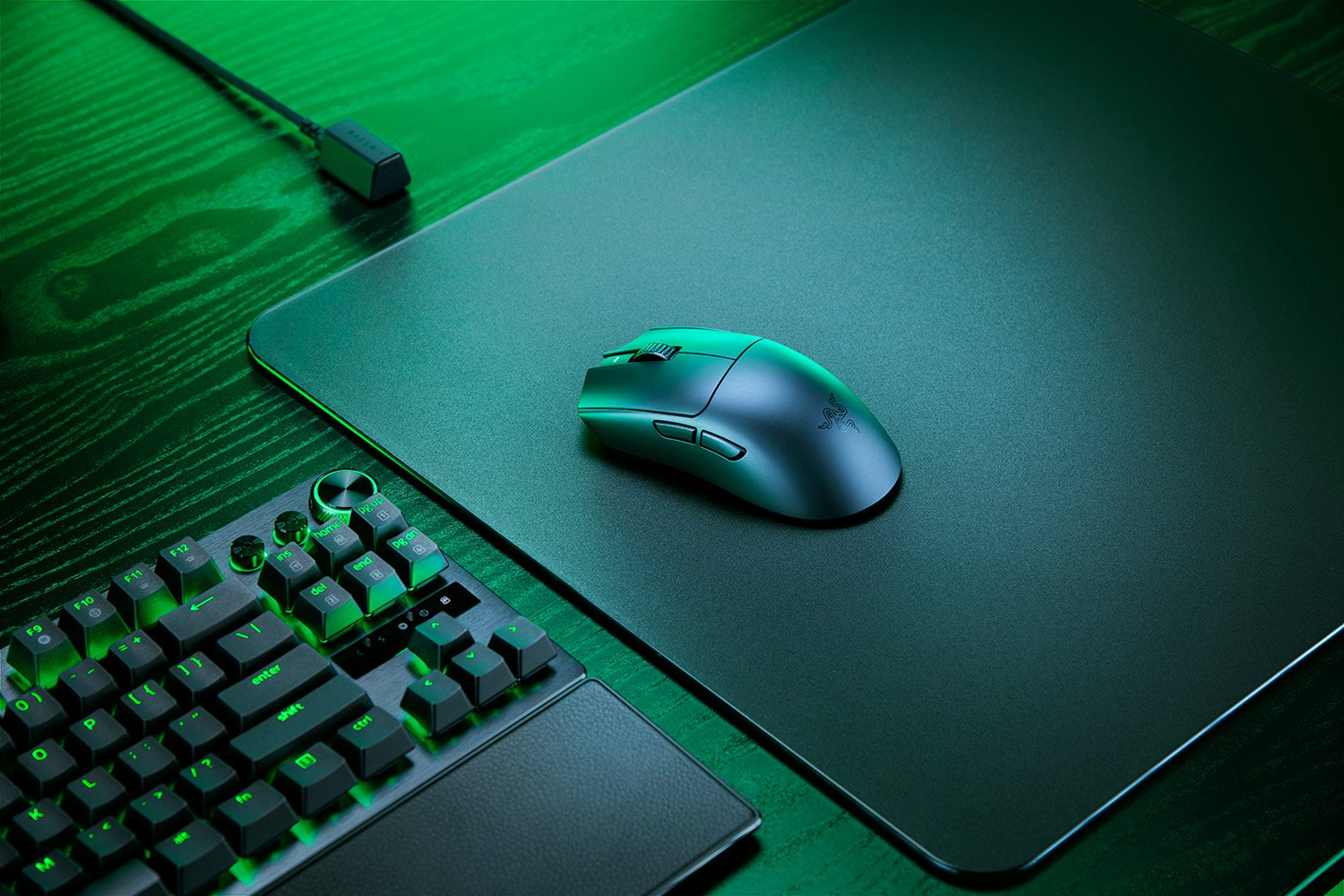 Black gaming mouse on a black mousepad, keyboard in the corner on a dark wood desk.