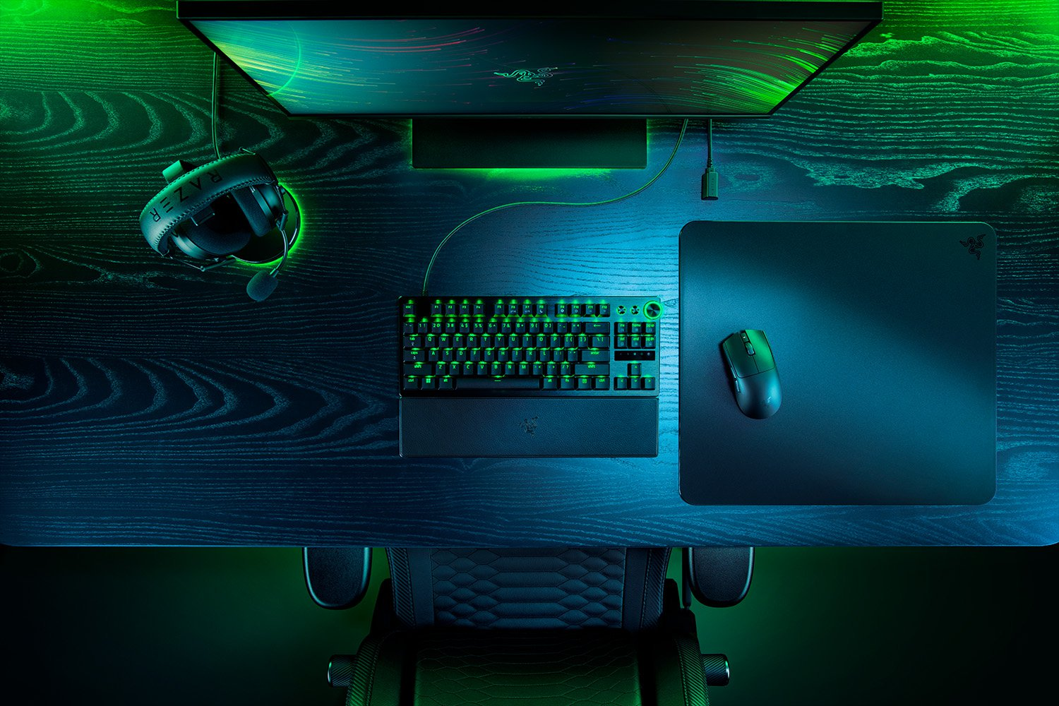 Gaming setup with monitor, headphones, keyboard, mouse, and mousepad. The setup is on a dark wooden desk.