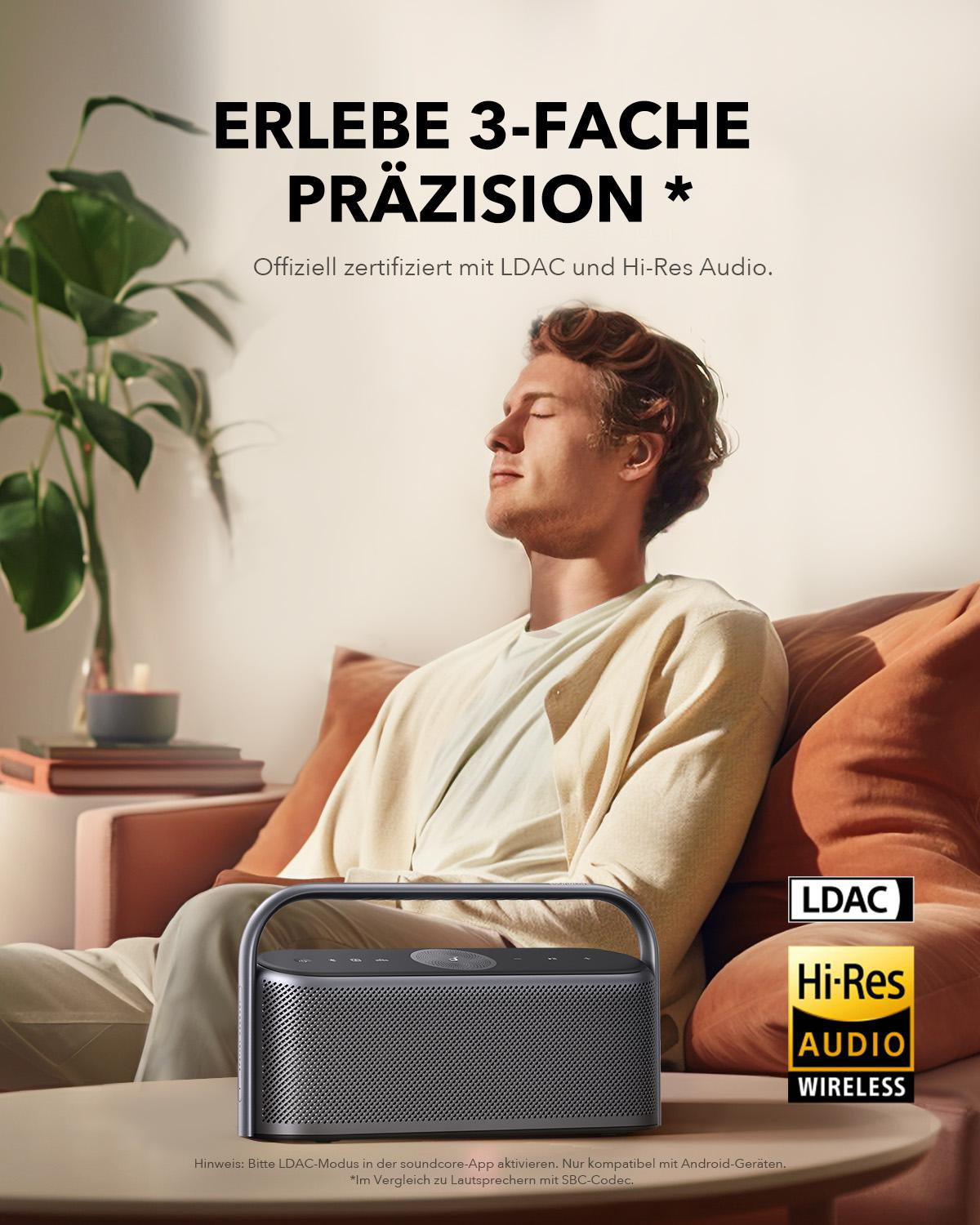 Mann sitzt auf einem Sofa und hört Musik über einen Lautsprecher. Text: 'ERLEBE 3-FACHE PRÄZISION'.