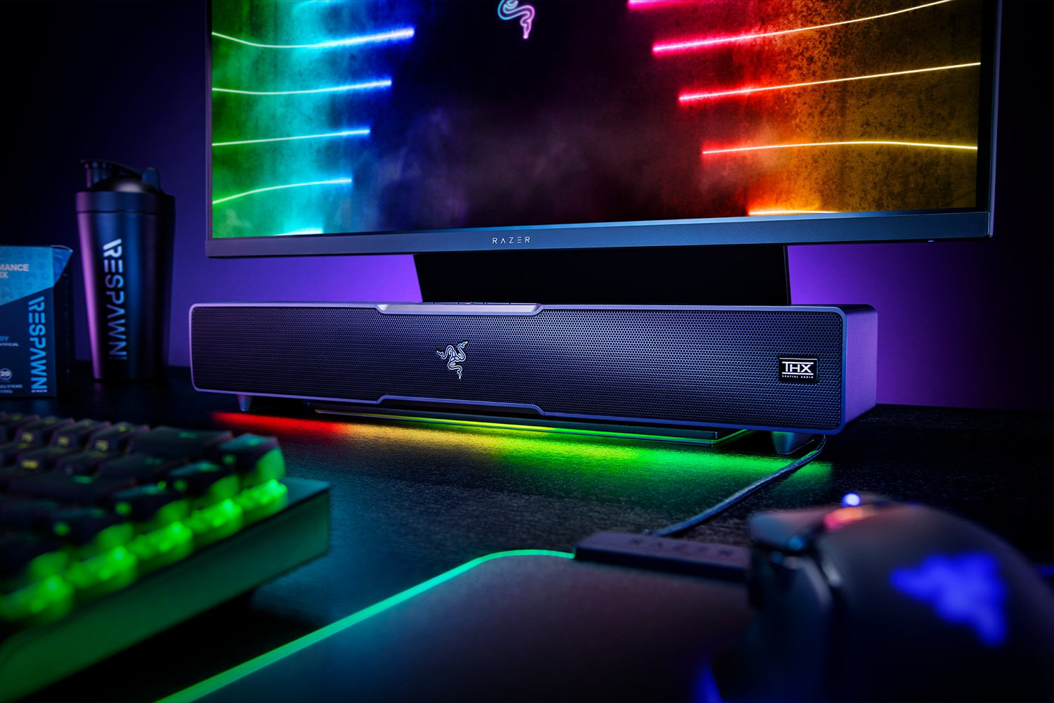 Een gaming setup met een monitor en Razer soundbar, toetsenbord en muis op een bureau.