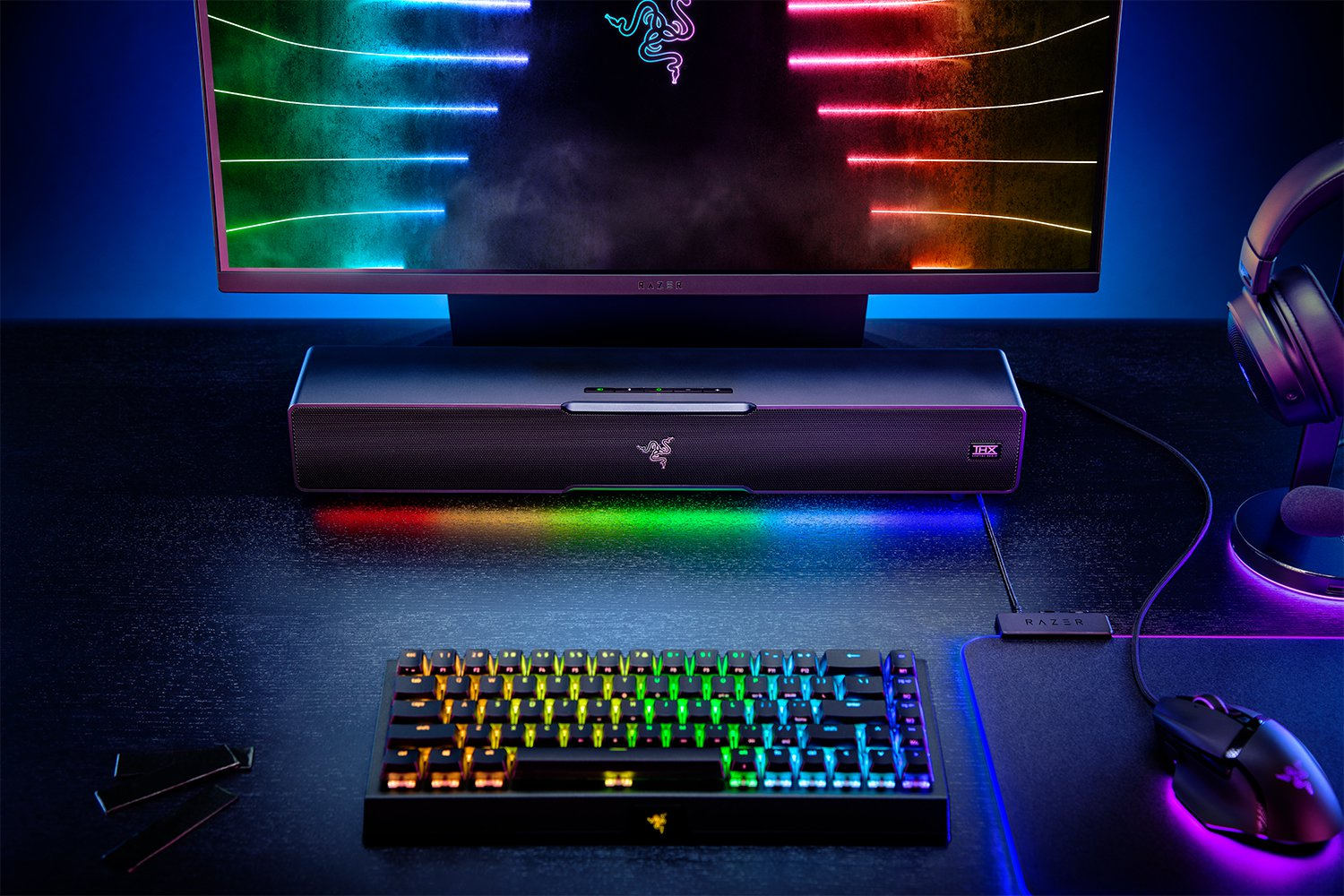 Gaming setup met een Razer toetsenbord, monitor en soundbar. Kleurrijke lichten.