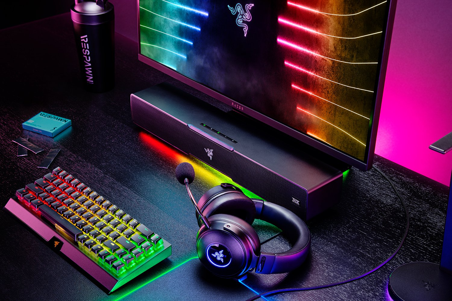 Gaming setup met toetsenbord, headset, monitor en luidspreker, allemaal met RGB-verlichting.